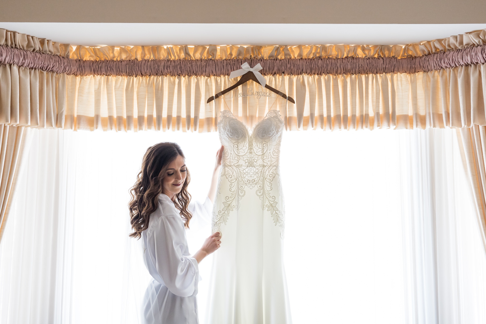 bride holding her dress in front of a window