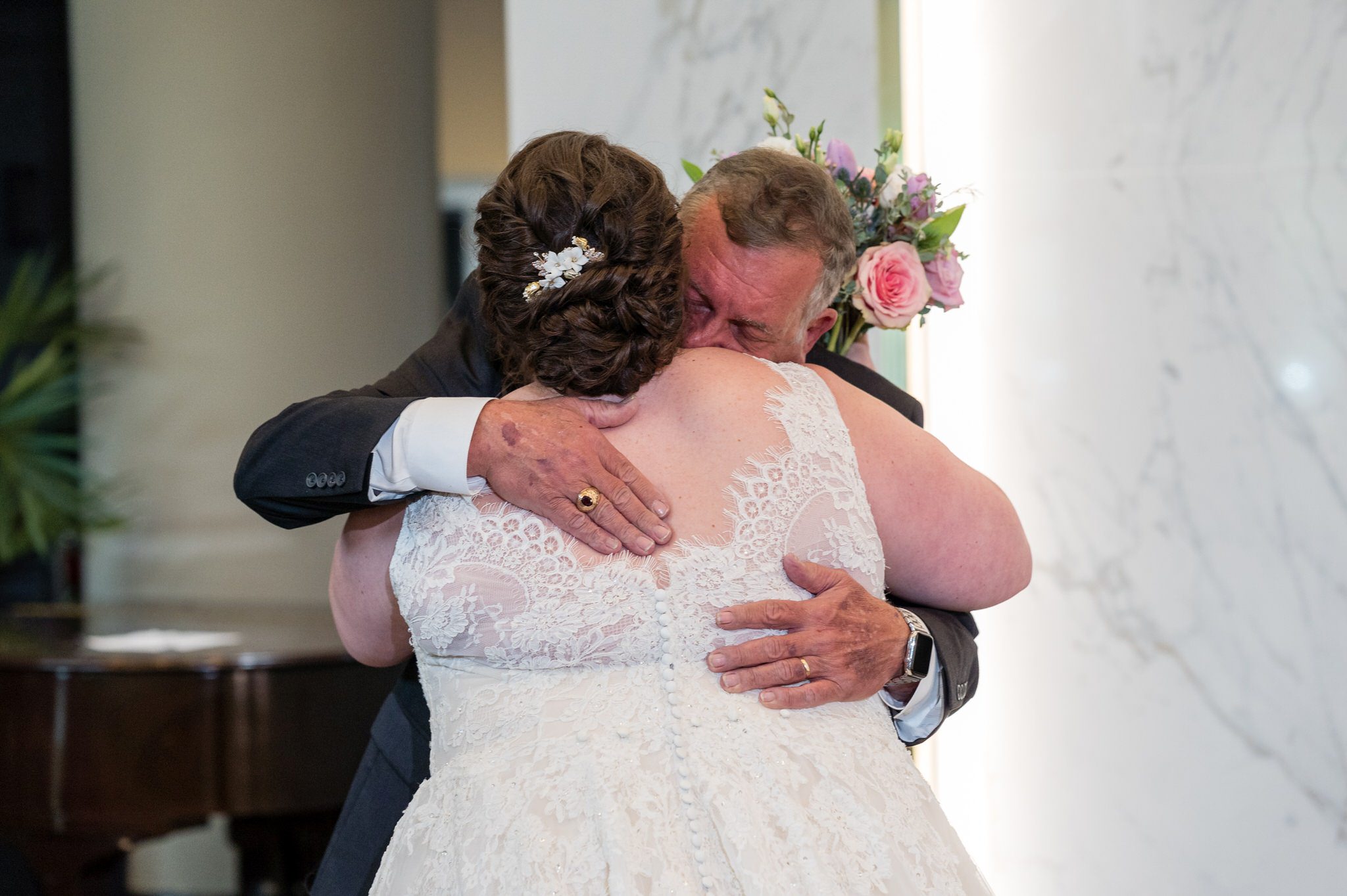 a father hugs his daughter on her wedding day in the lobby of the Atheneum hotel