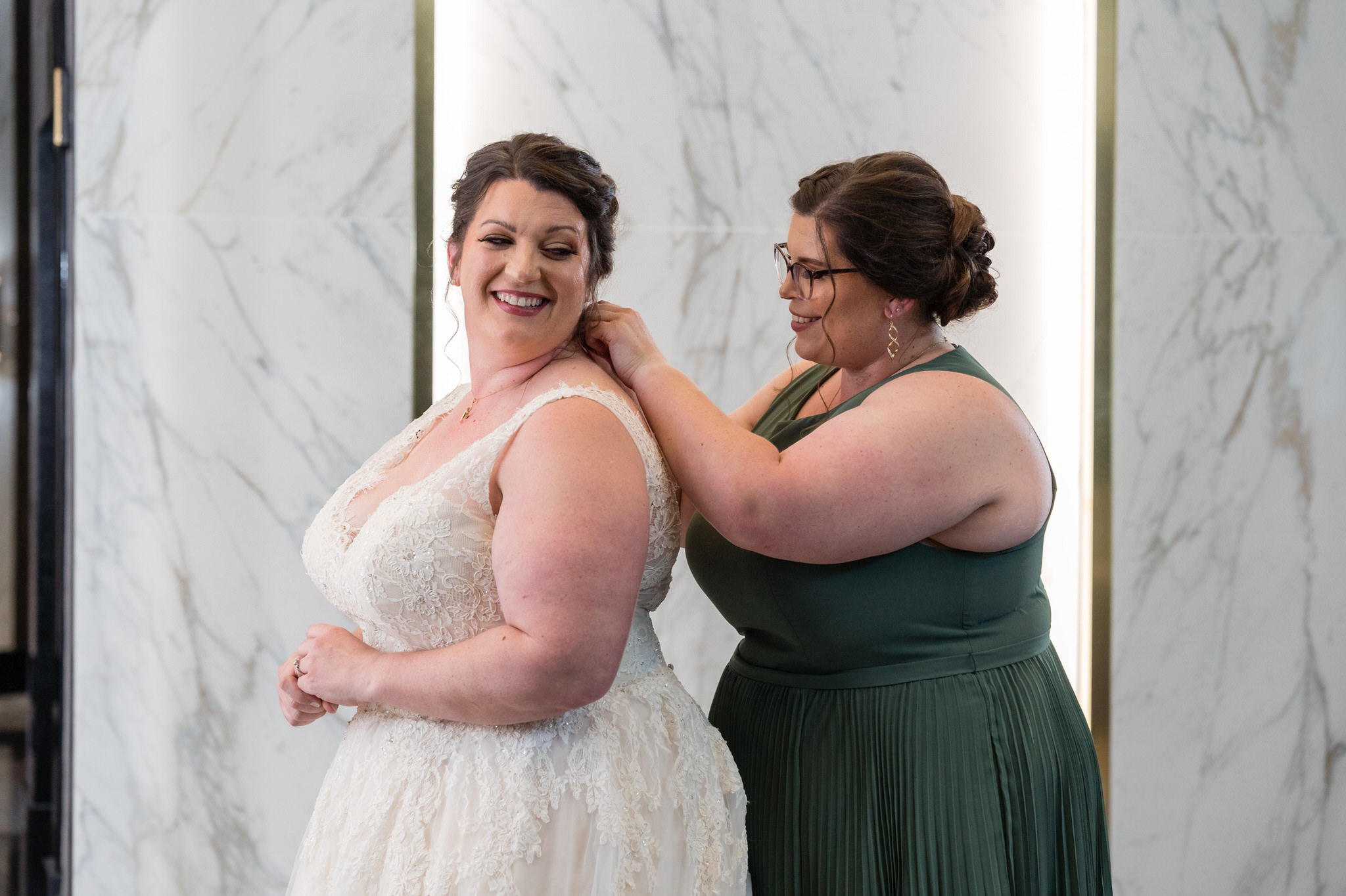 a bride gets ready with the help of her bridesmaid