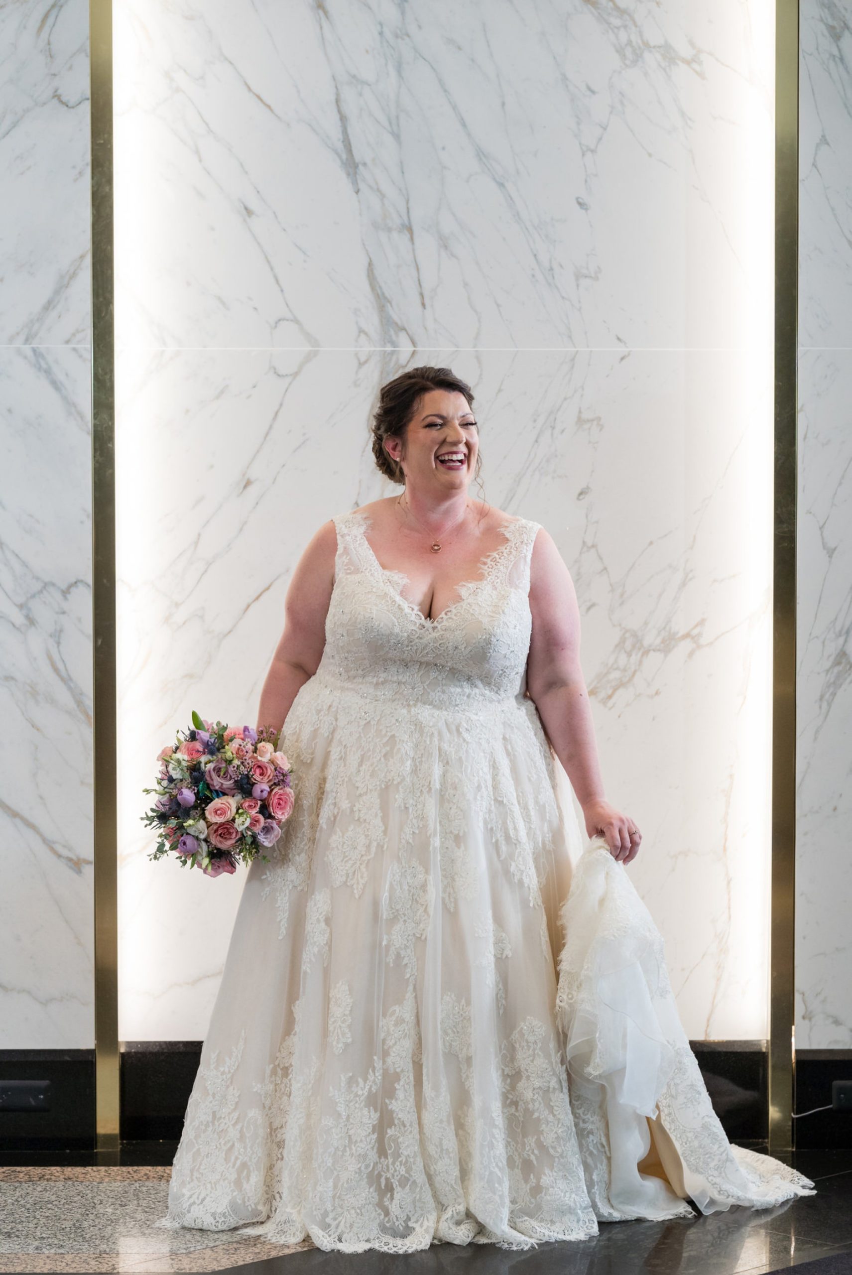 a bride laughs while holding her dress in the lobby of the Atheneum Hotel in Detroit