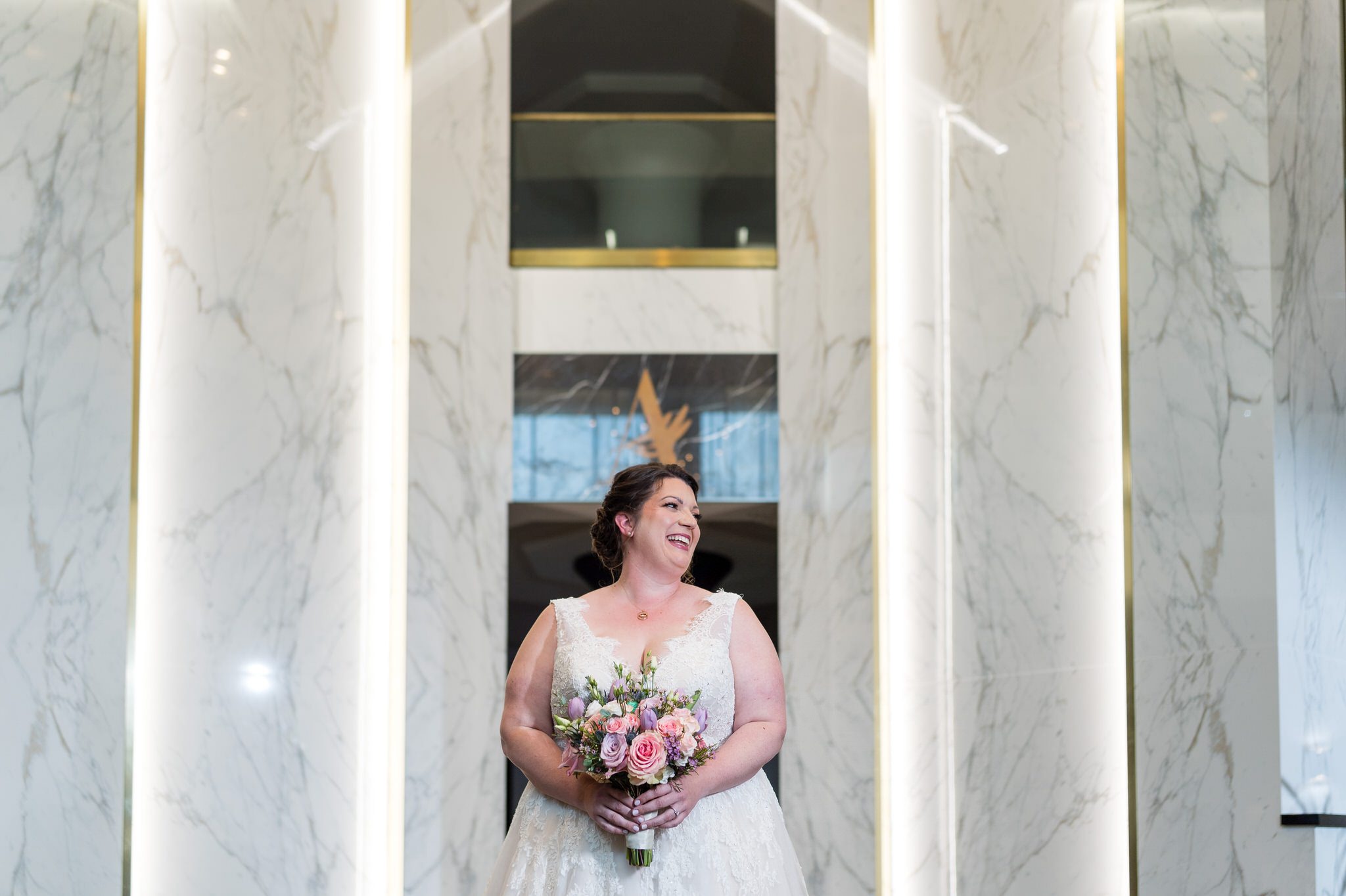 a bride smiles while holding a bouquet in the lobby of the Atheneum Hotel in Detroit