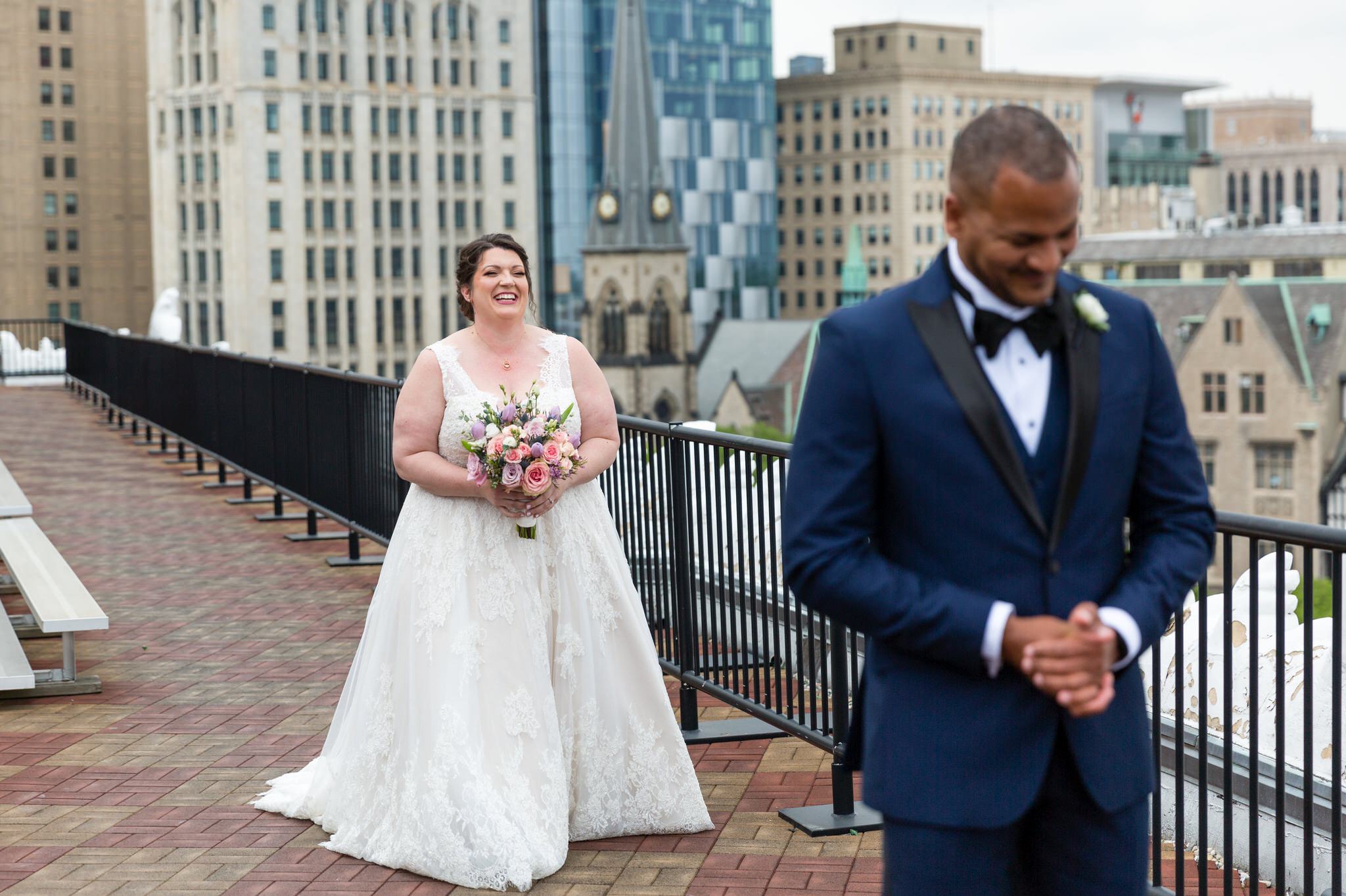 a bride approaches her groom with the Detroit skyline in the background