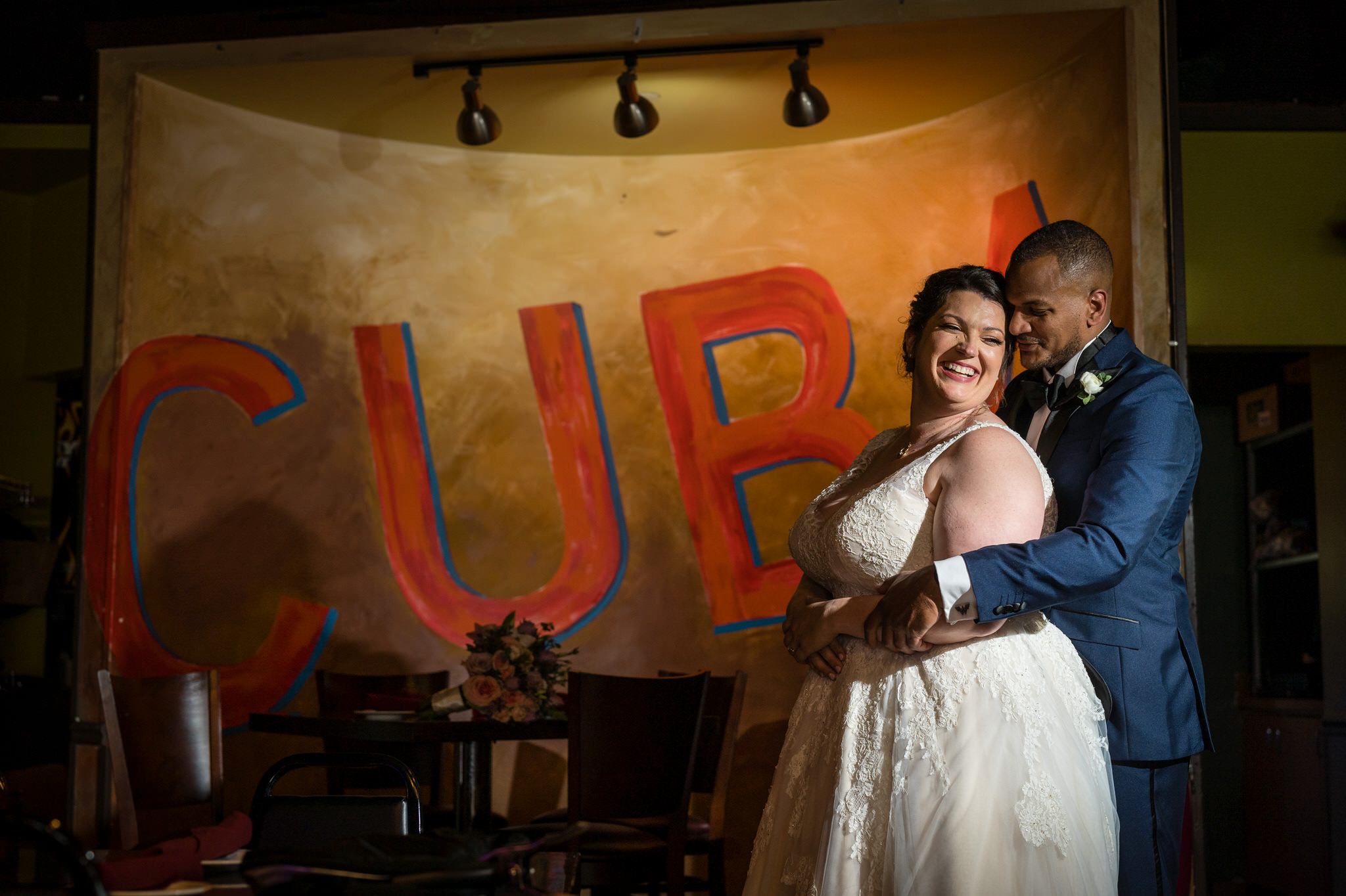 a groom hugs a bride from behind with a red Cuba sign behind them