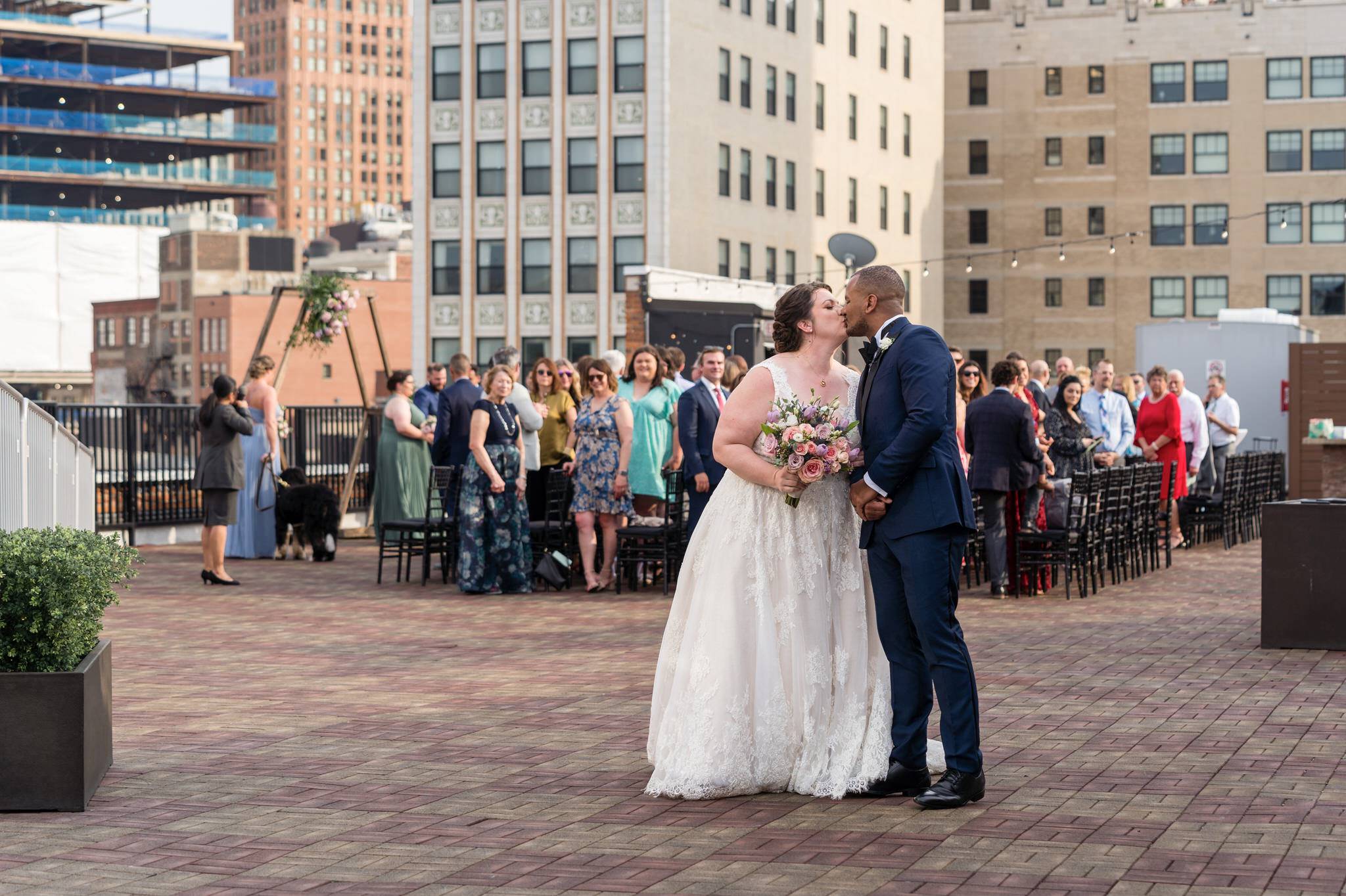 bride and groom kiss with guests behind them at their rooftop wedding at the Detroit Opera House