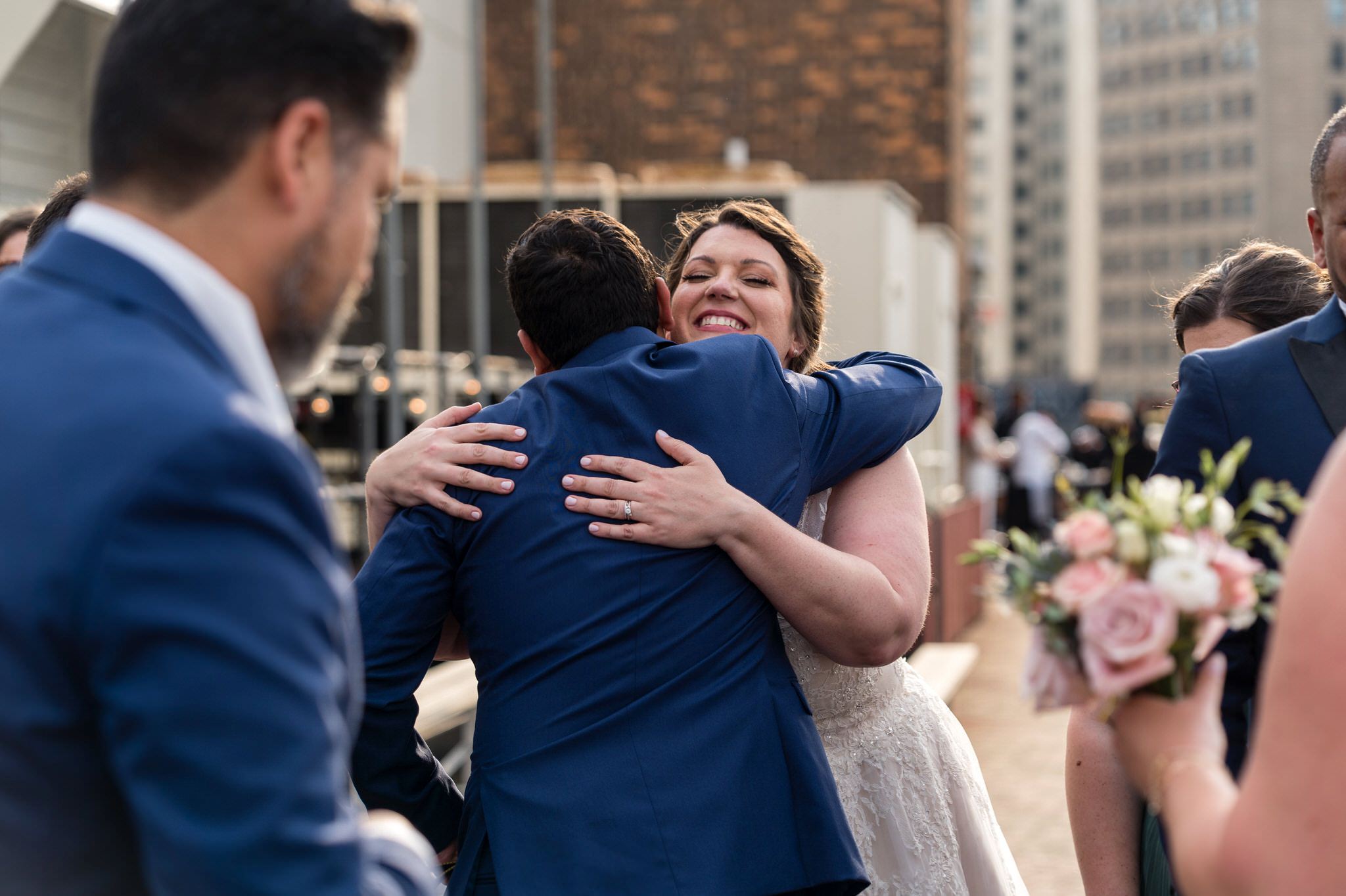  a bride hugs a groomsman after getting married at their rooftop wedding at the Detroit Opera House