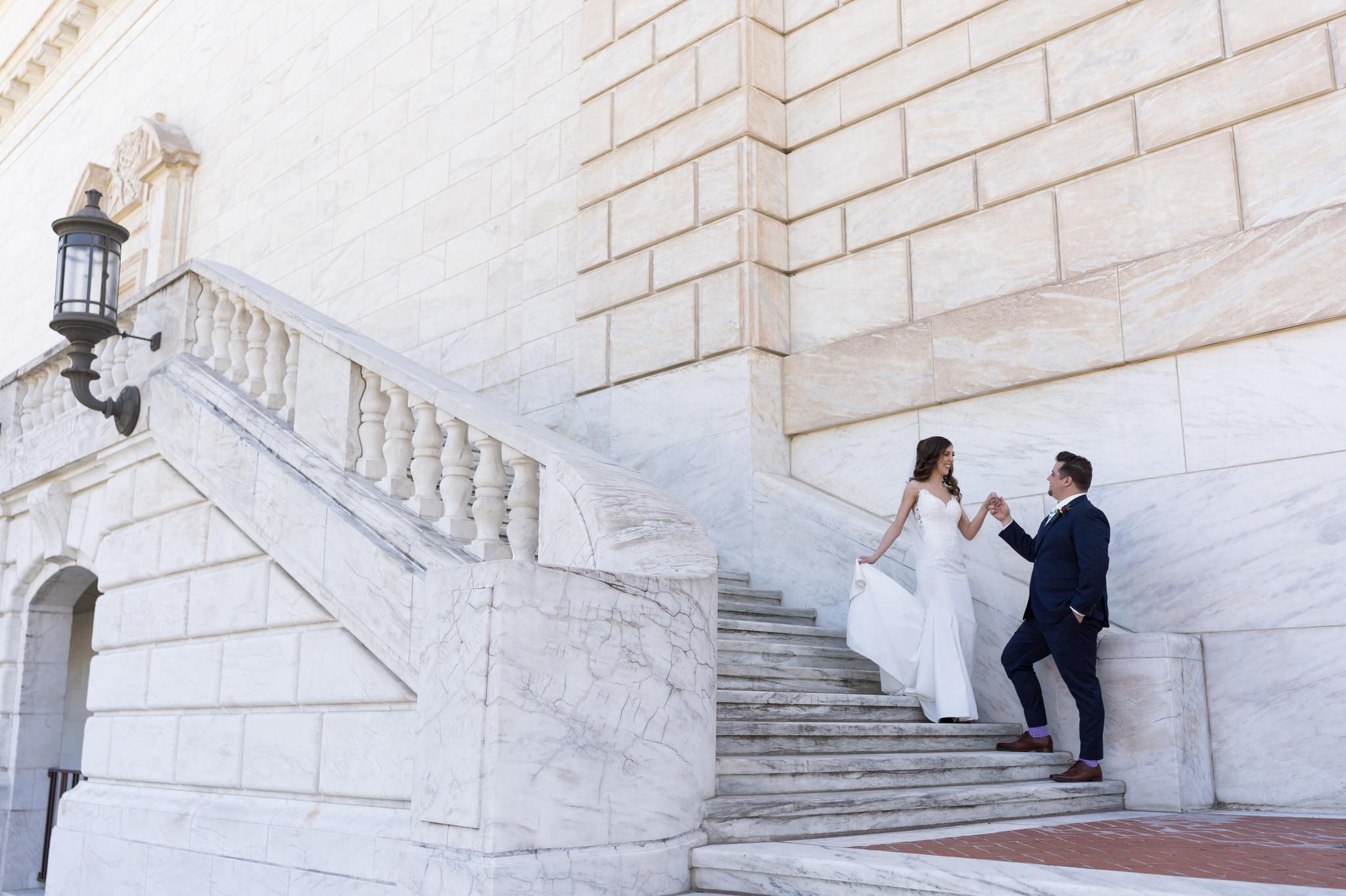 groom holding brides hand and helping her walk down the stairs at the Detroit Institute of Arts