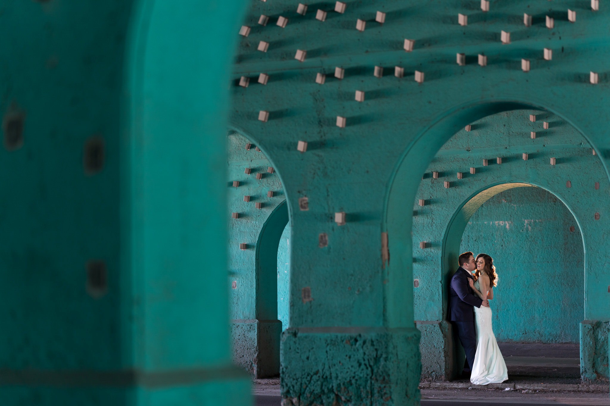 groom kissing bride's cheek under a green archway in Midtown Detroit