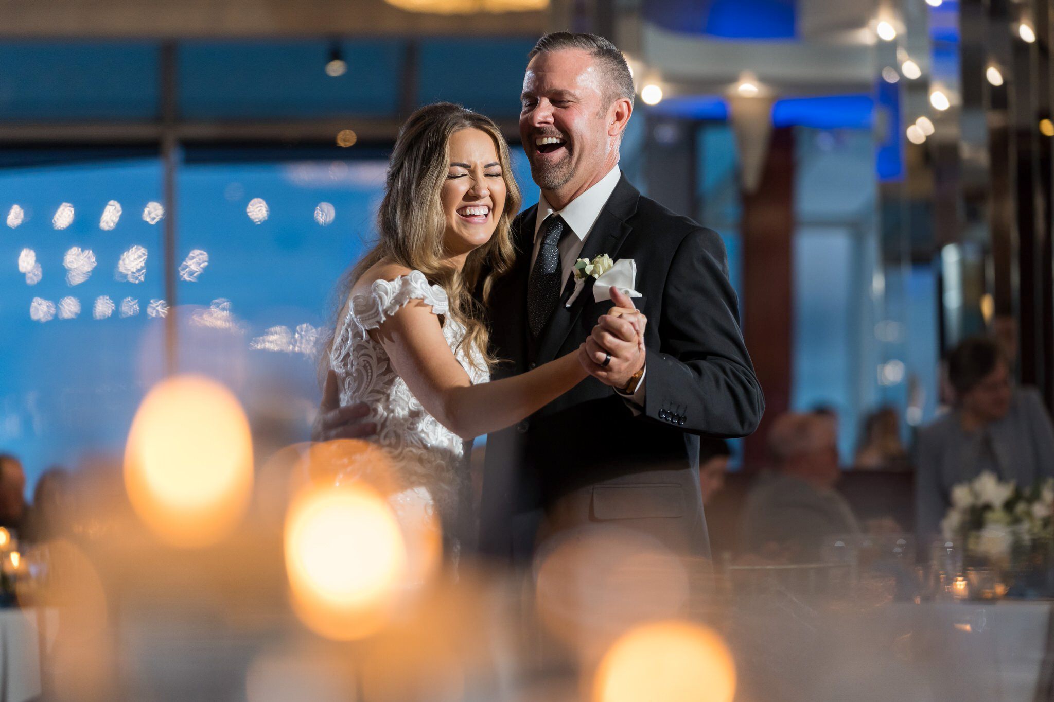 Father of the bride dances with his daughter with candlelight in the foreground during MacRay Harbor wedding reception