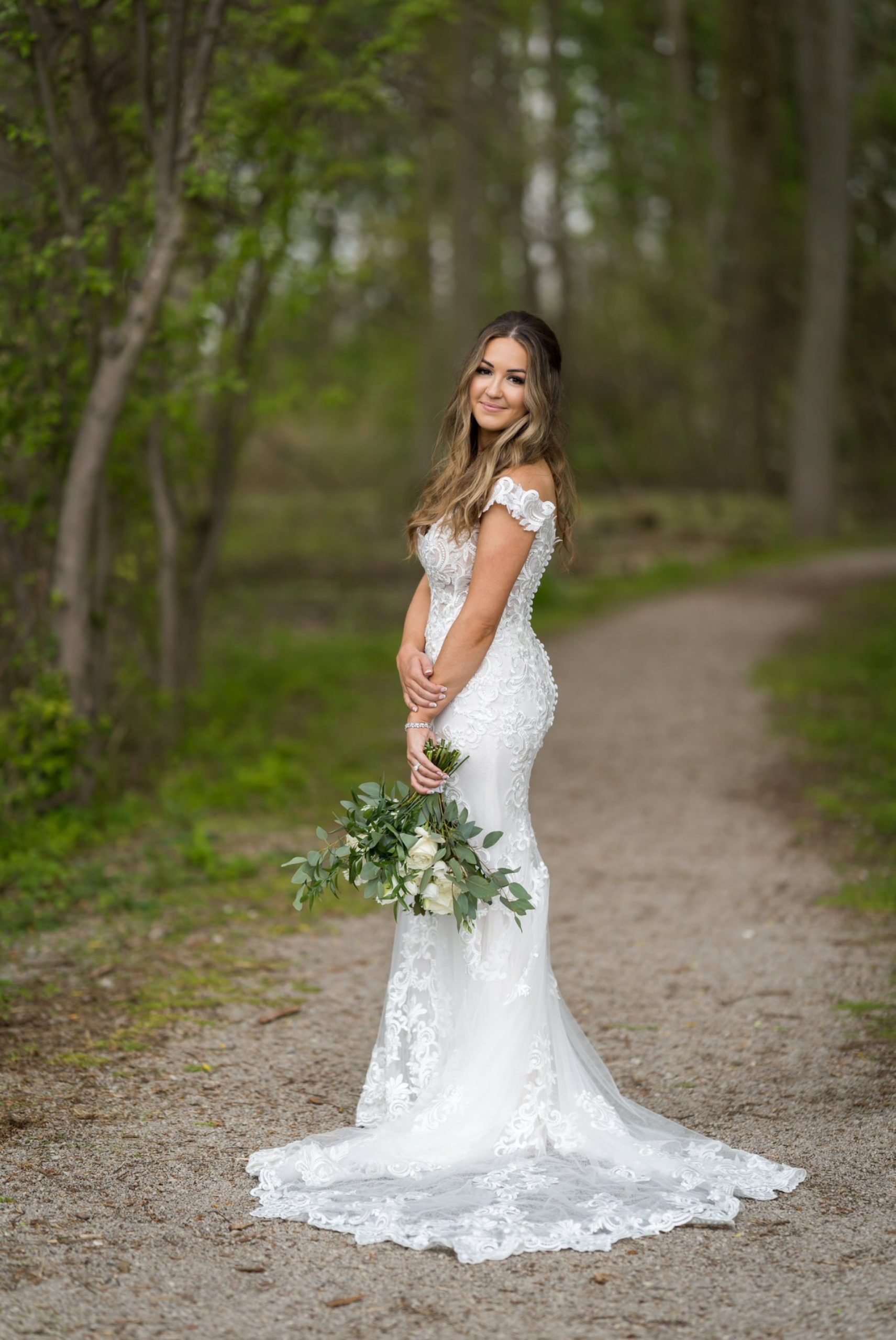 a bride poses in nature while holding her arm and white rose bouquet