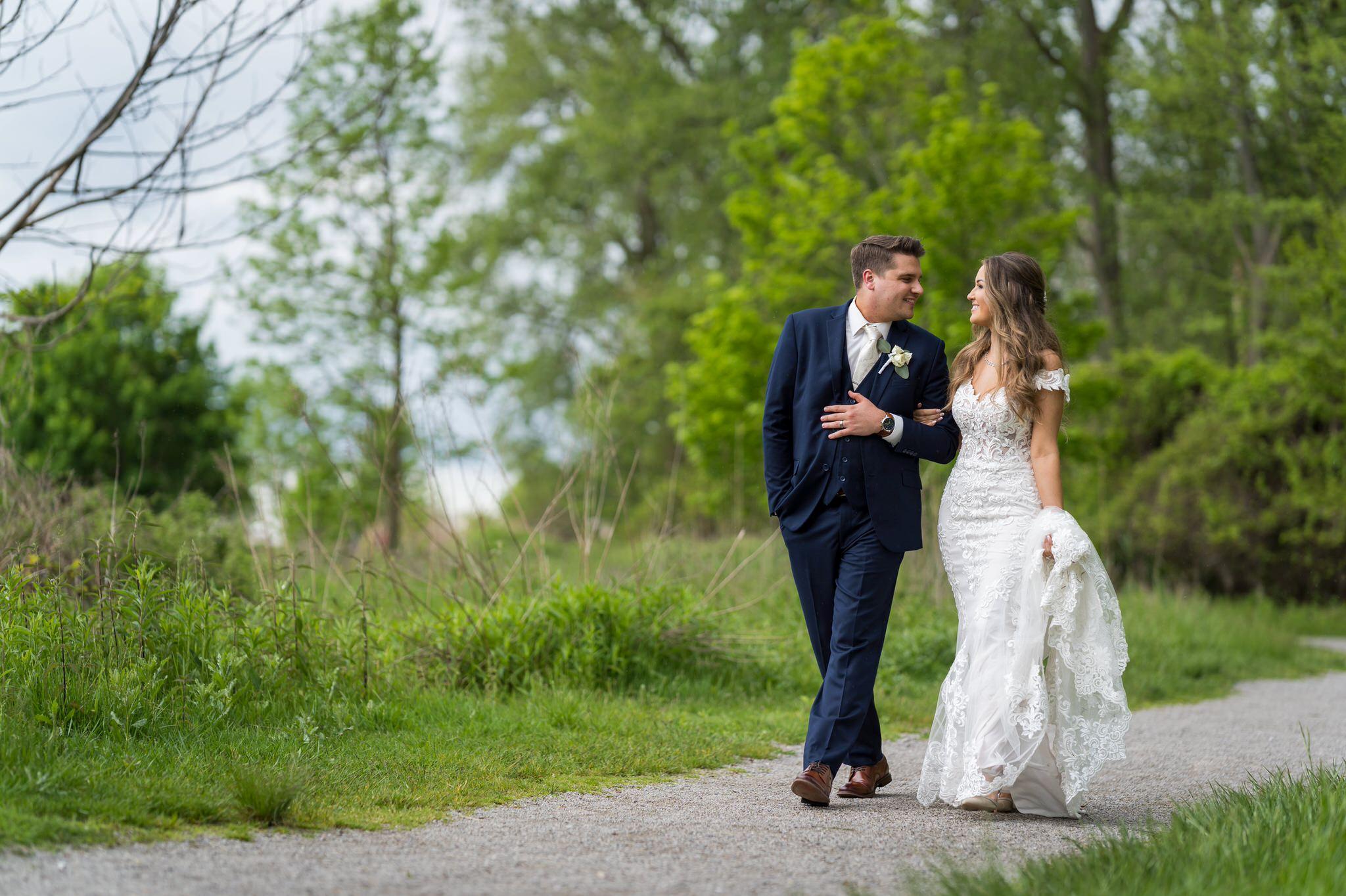 bride and groom walking on dirt path with greenery around them
