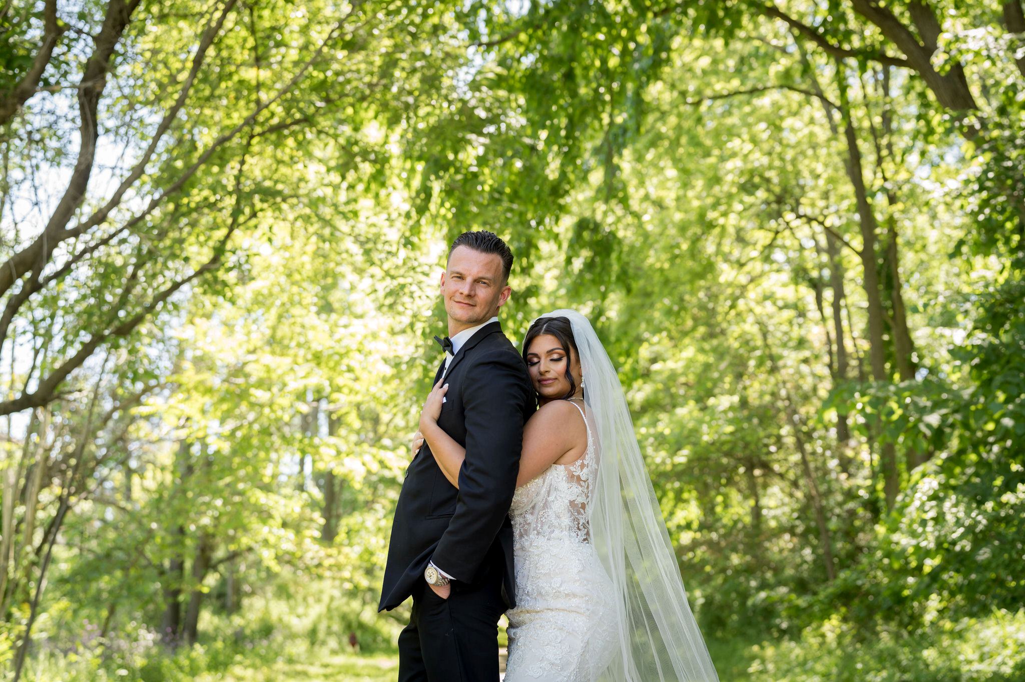 a bride holds the groom from behind in a walking path at Van Hoosen