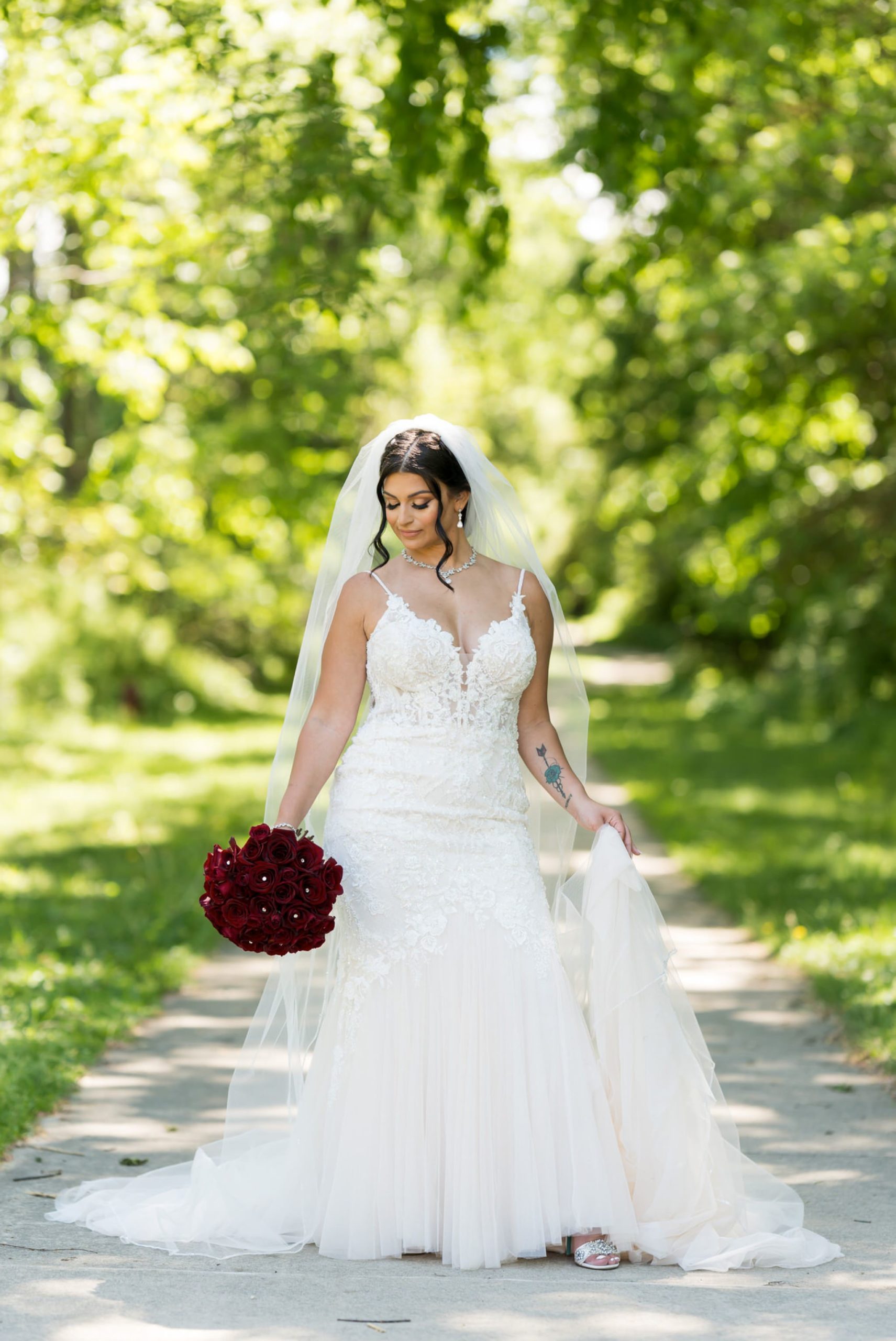 a bride holds her dress in a walking path at Van Hoosen