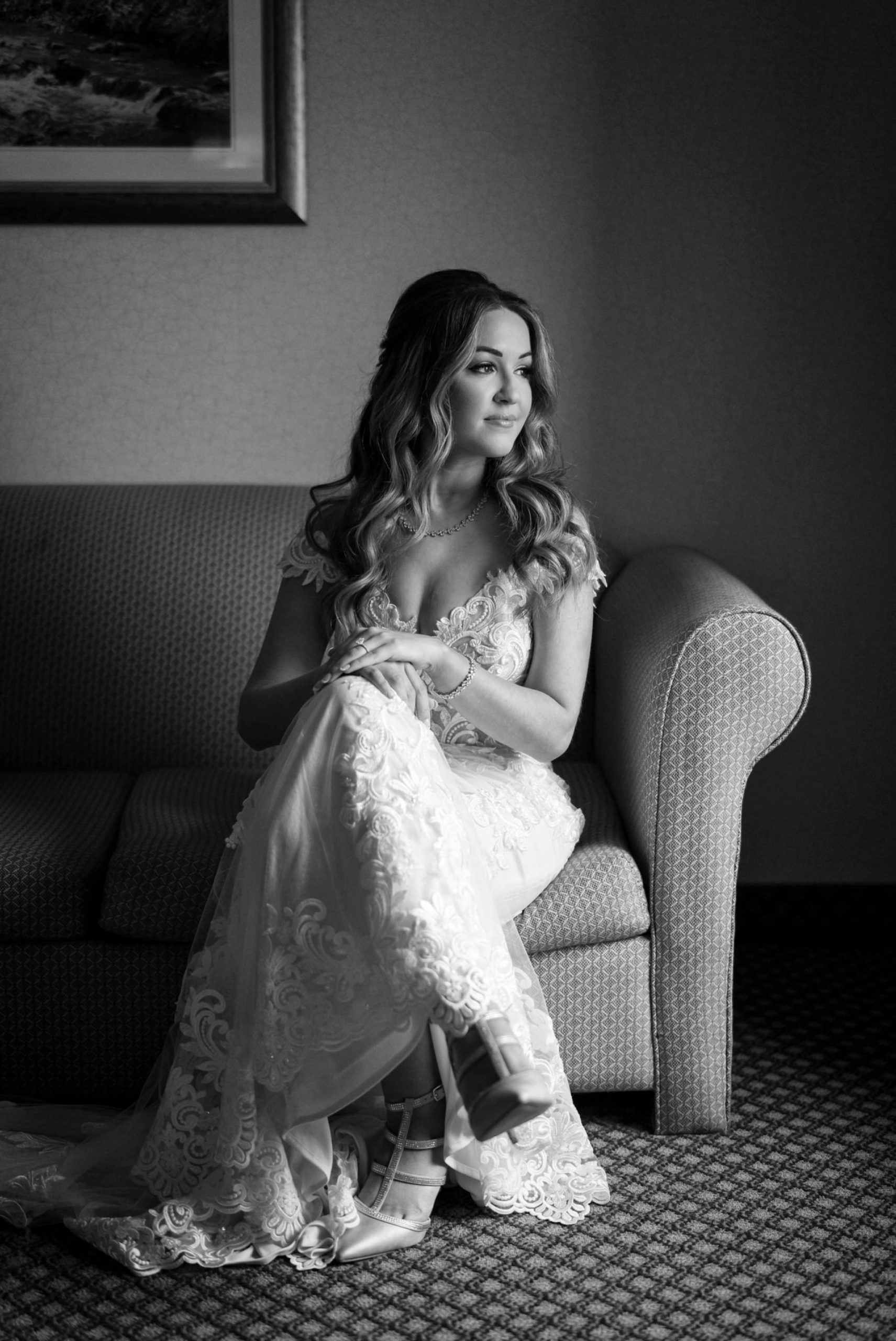 a bride, sits on a couch with her hands on her knee, looking out the window