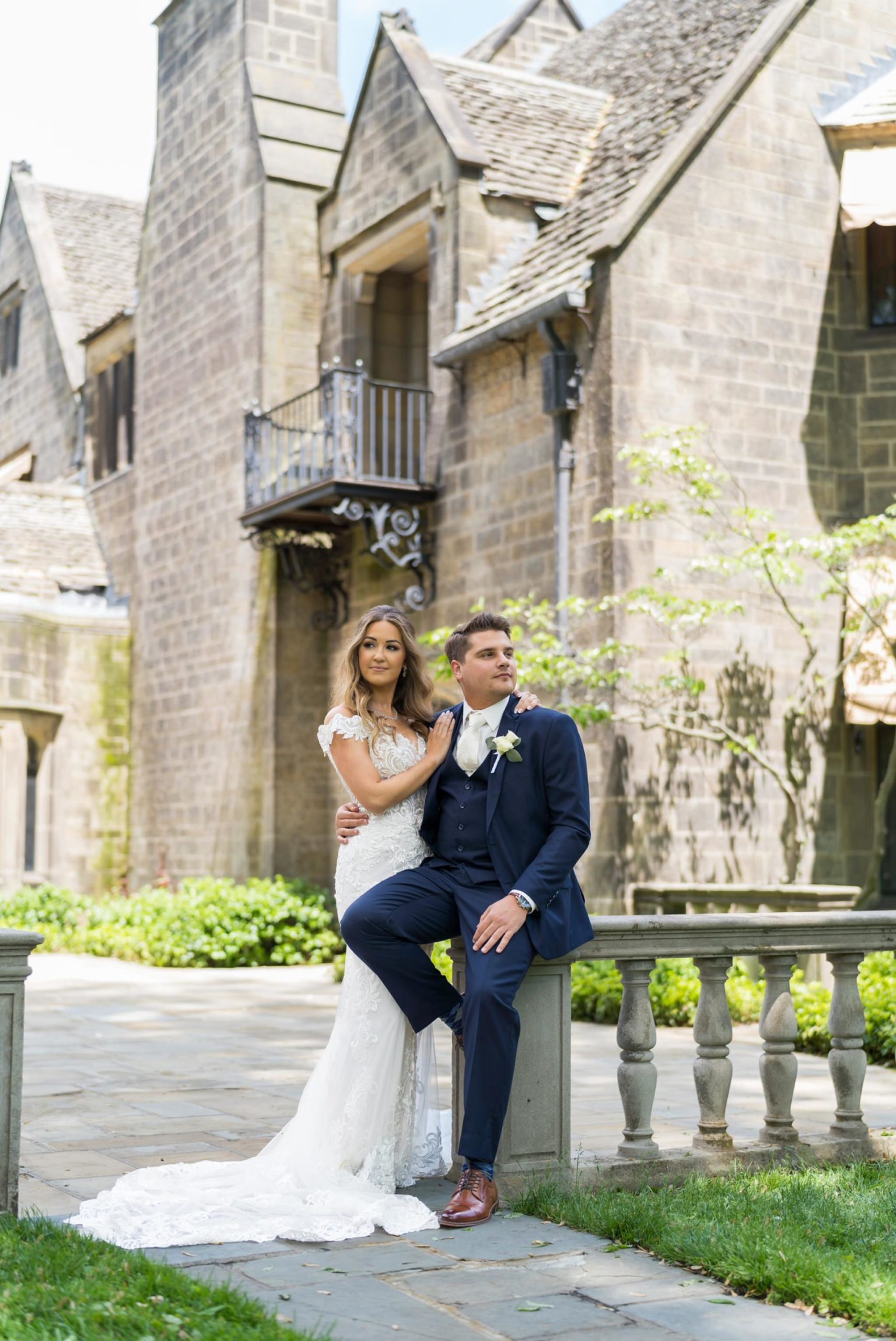 Groom sits on a railing while the bride holds him at the Edsel Ford House