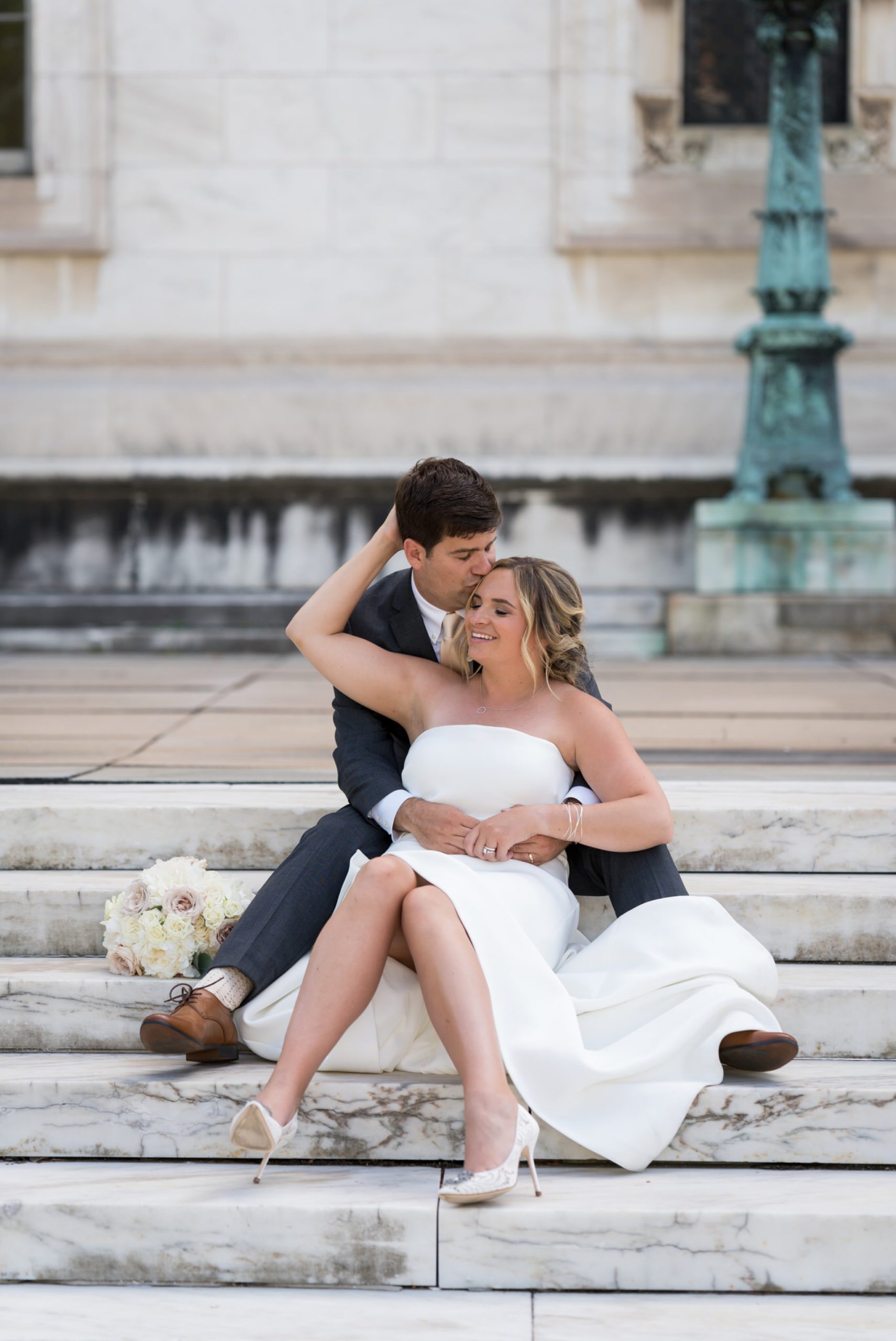 bride and groom sit on the steps of the detroit public library 