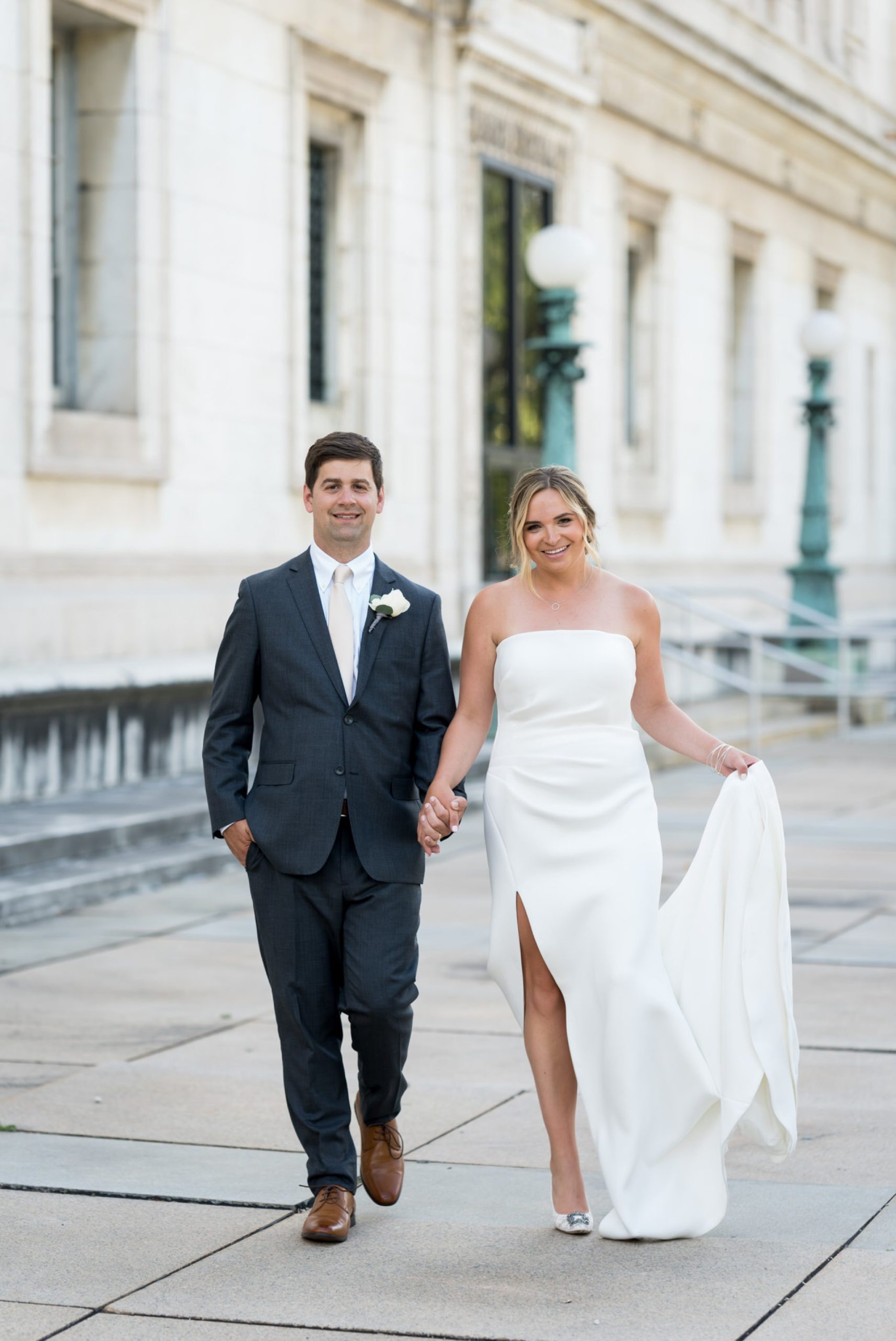 bride hold her dress as she walks with her groom at the Detroit Public Library