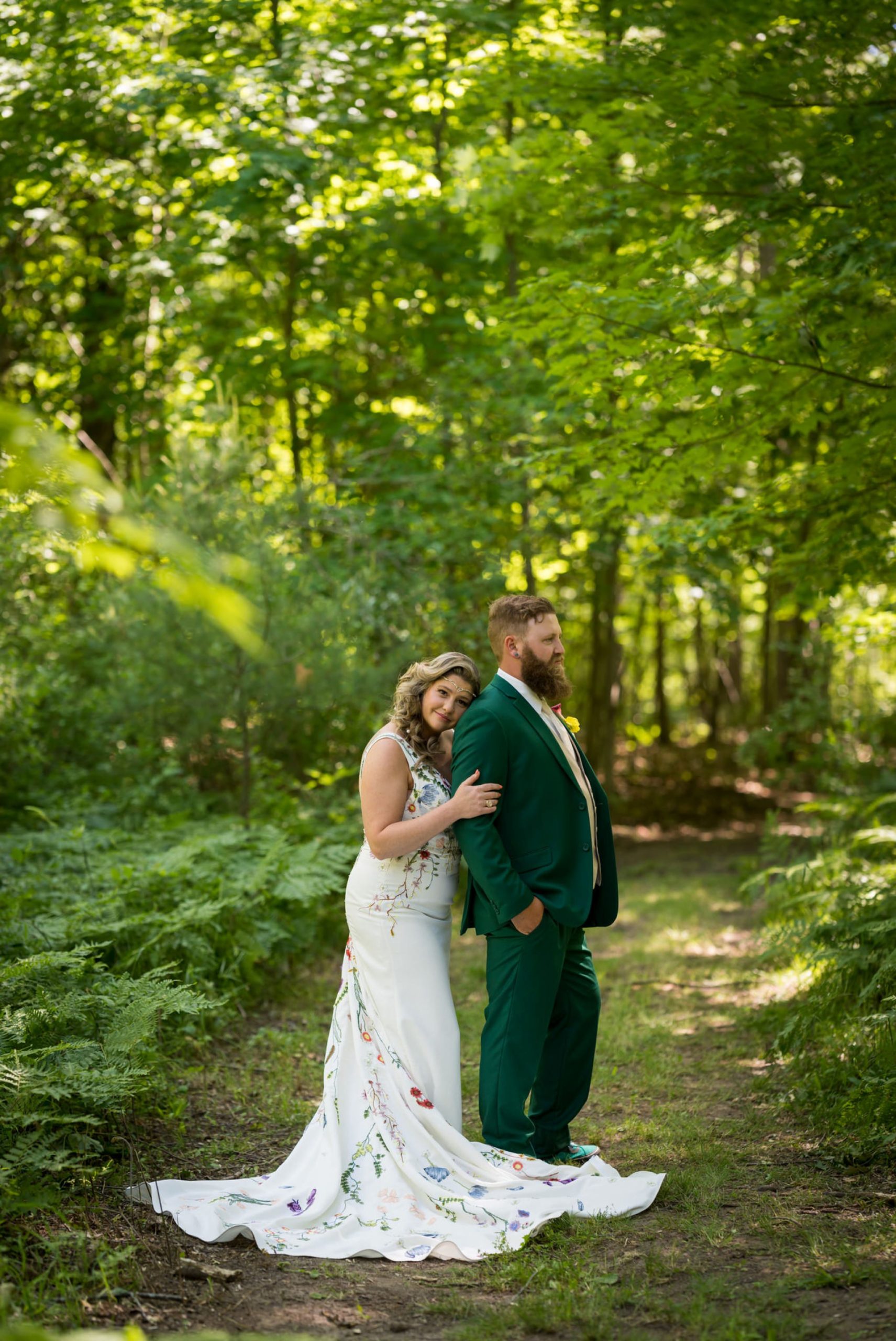 bride hugs groom from behind on a path in the woods on their wedding day
