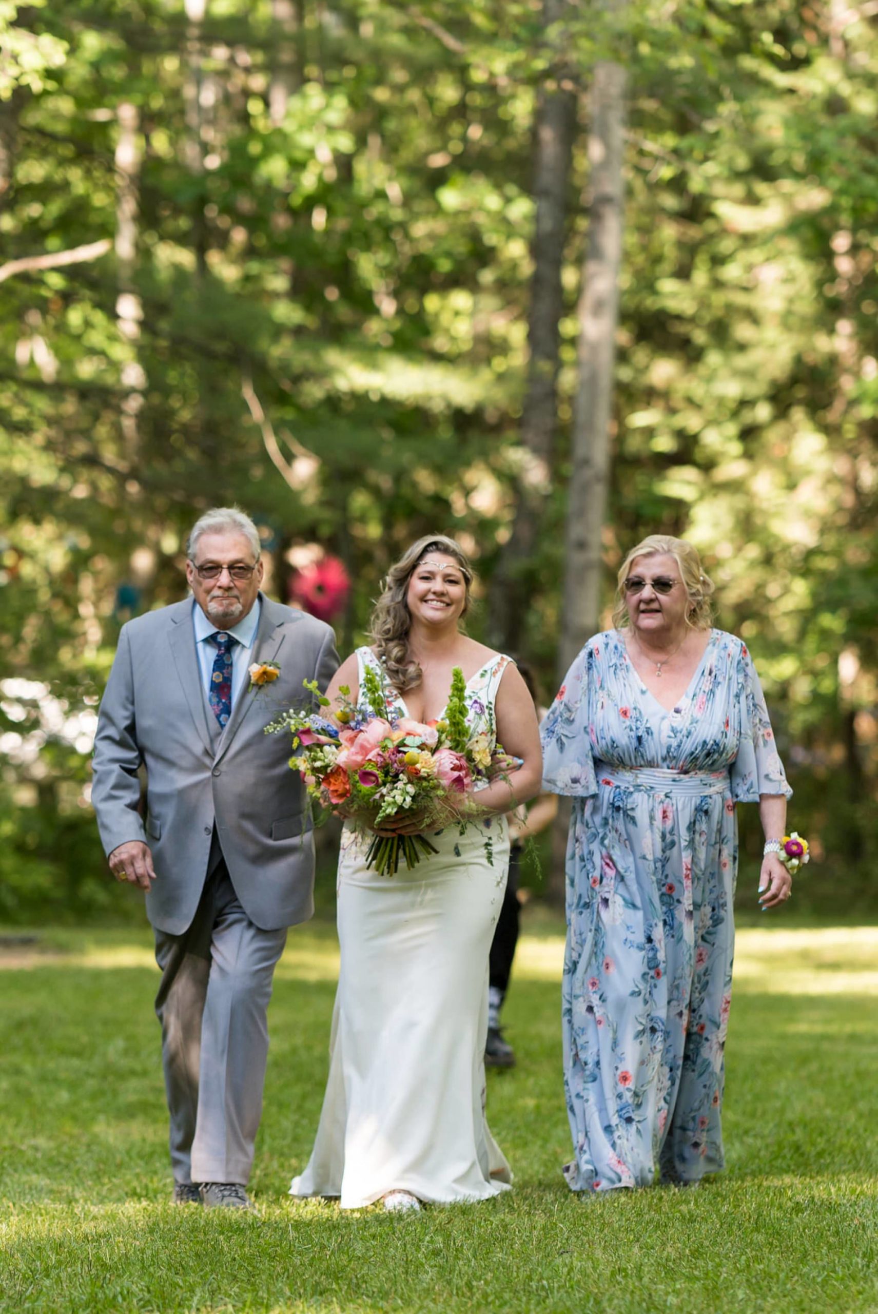 a bride is escorted by her father and mother in an outdoor wedding