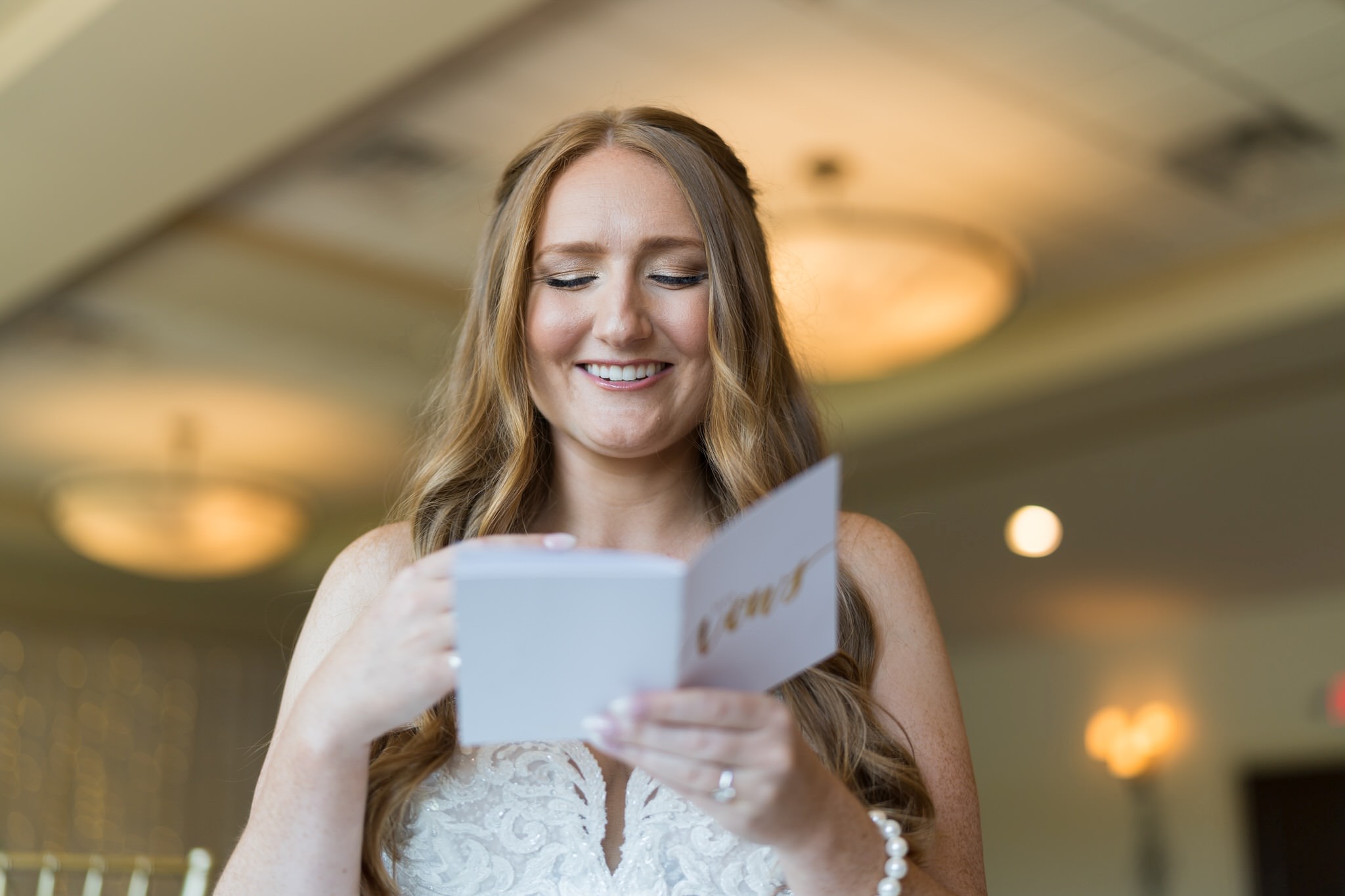 A bride smiles as she reads a letter from her groom before their Greystone Golf Club wedding. 