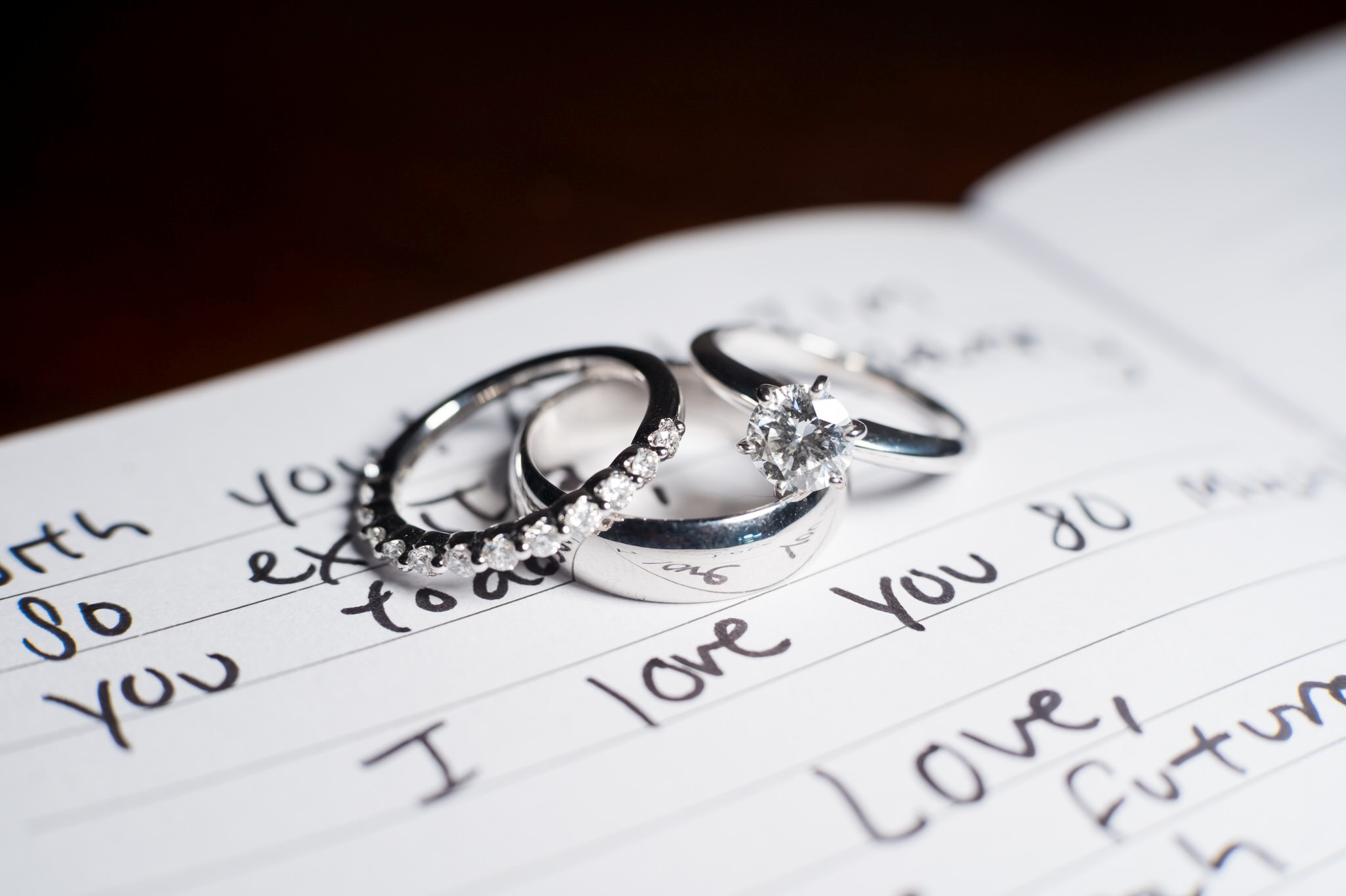 Three wedding rings balancing on a hand written note that reads "I love you."
