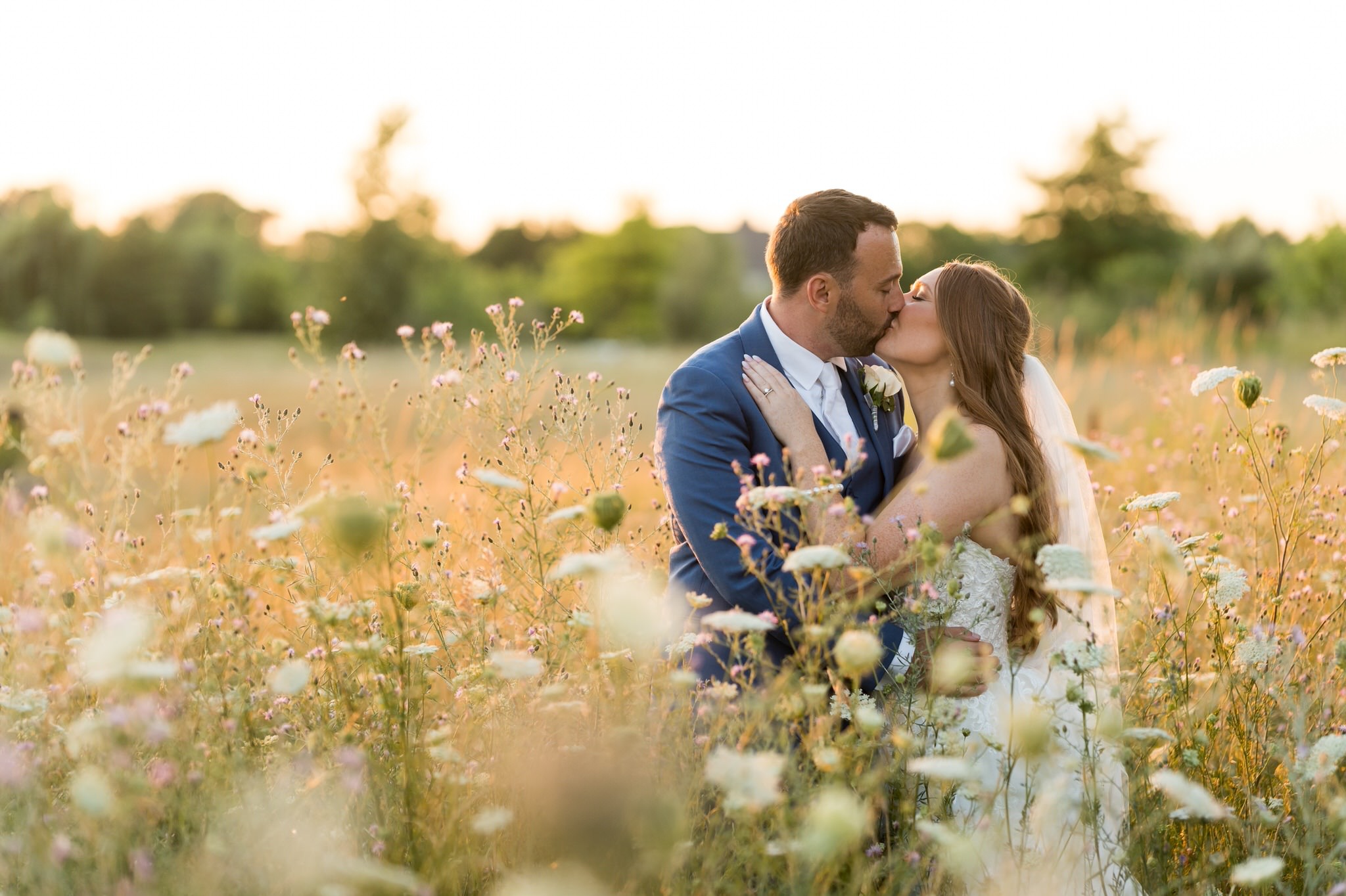 A bride and groom kiss in a field of wildflowers and tall grass during golden hour by Brian Weitzel Photography. 