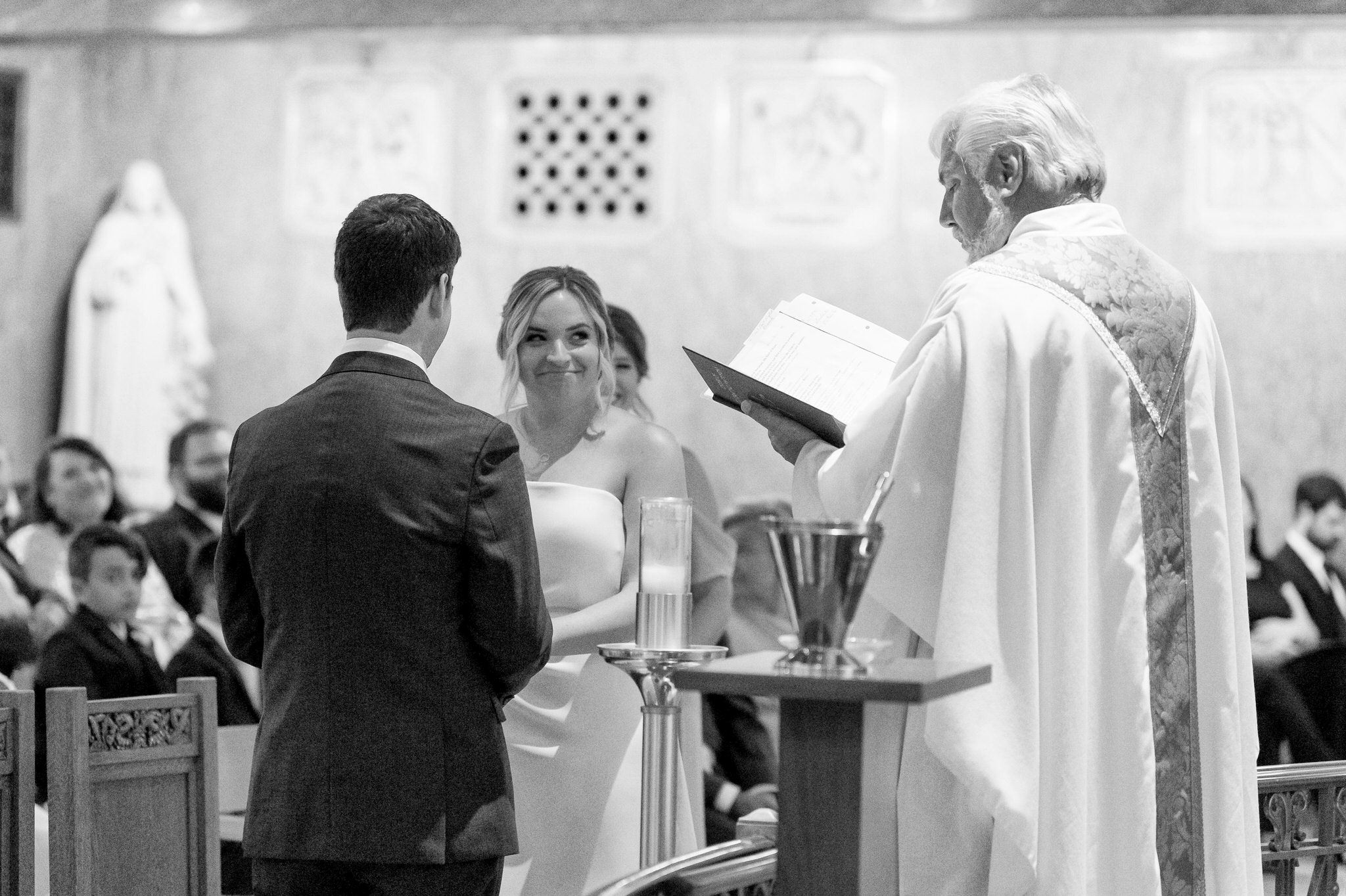 bride smiles at priest during vow exchange at St. Aloysius Church in Detroit 
