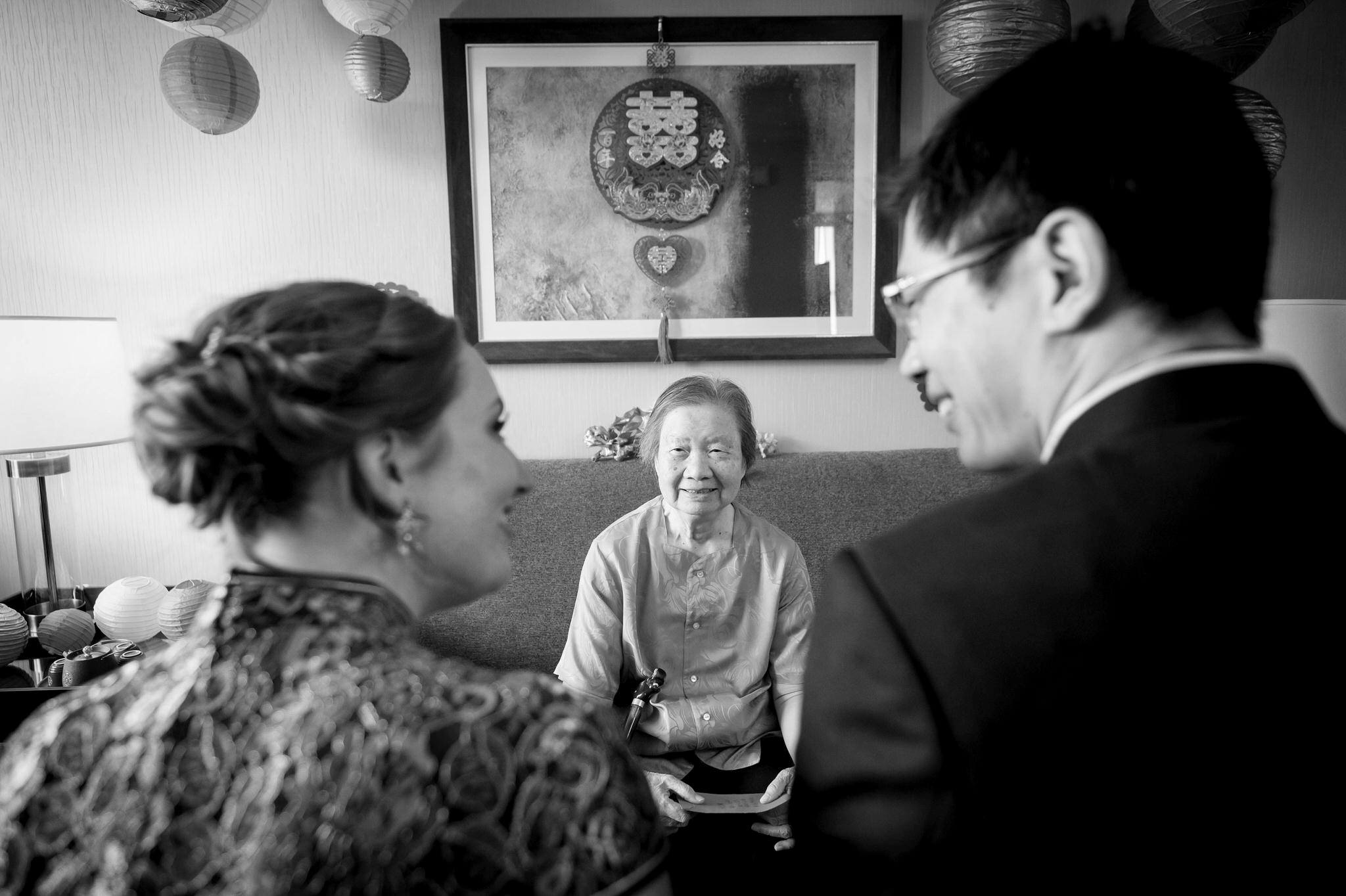 A bride and groom look at each other with grandma in between them during a Chinese wedding tea ceremony.  