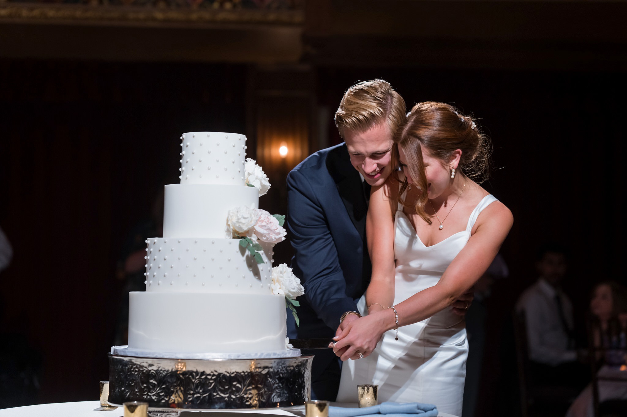 A bride and groom hug while cutting a wedding cake during their Gem Theatre Detroit wedding.  