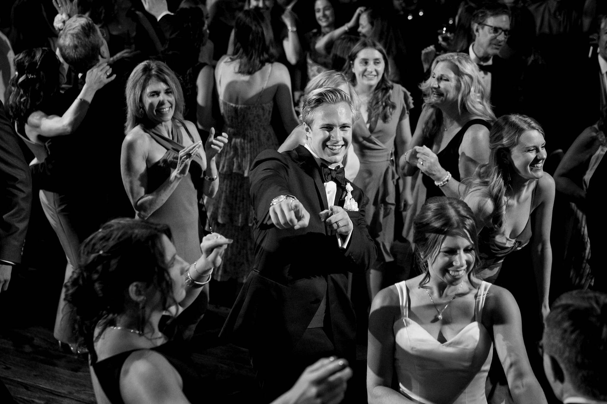 A groom wearing a tuxedo points to the camera on a crowded dance floor at a Gem Theatre Detroit wedding.  