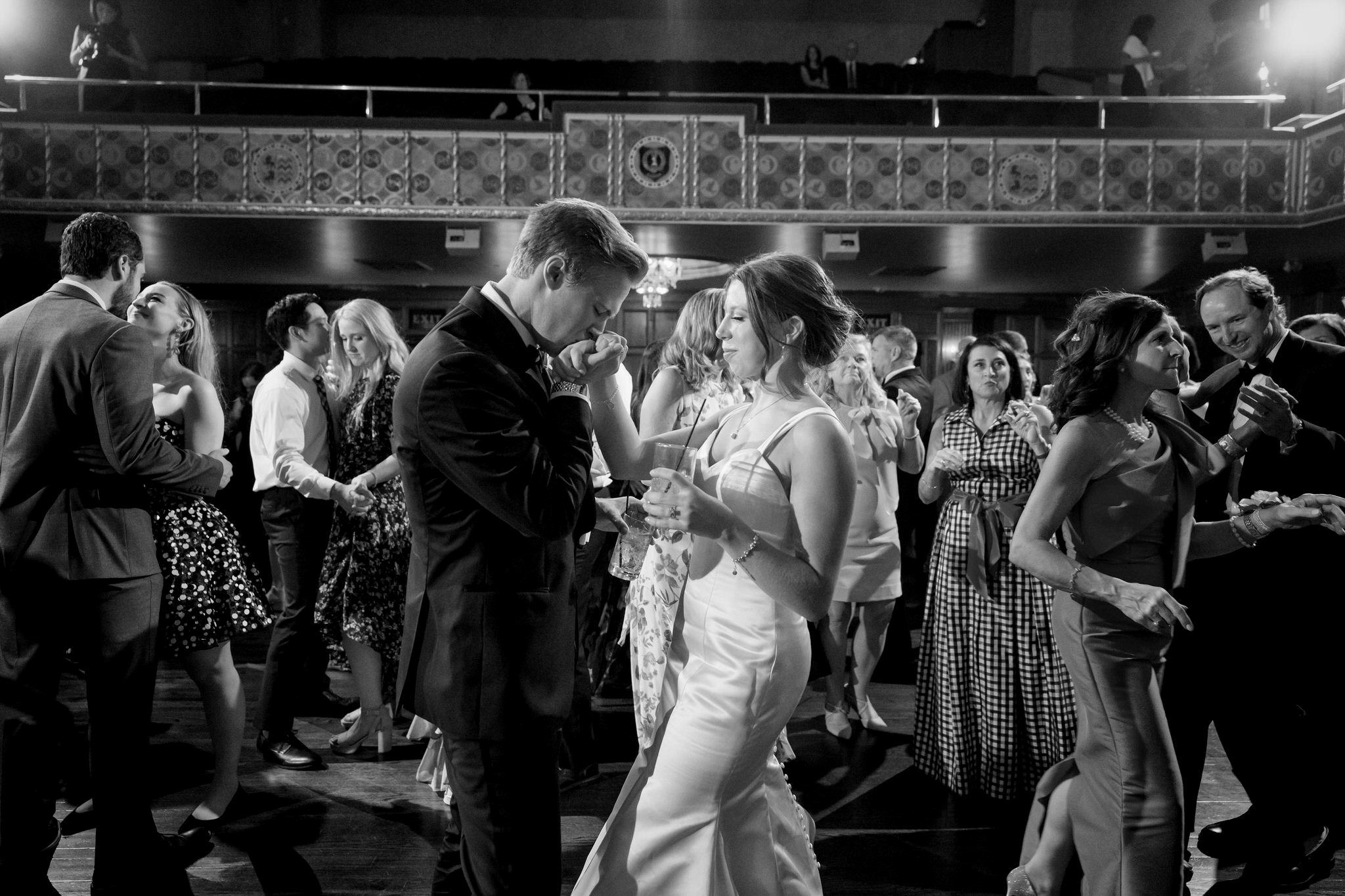A groom kiss the hand of his bride on a crowded dance floor at their Gem Theatre Detroit wedding. 