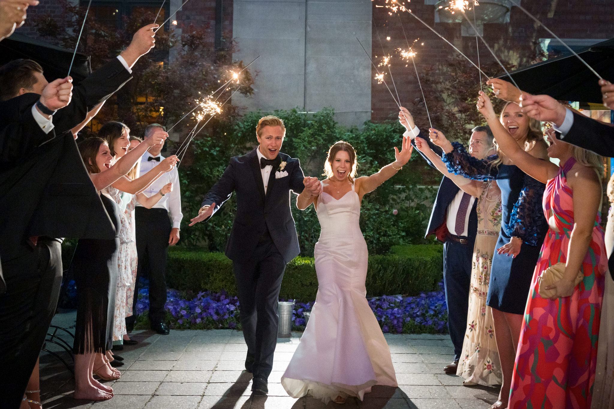 A bride and groom celebrate as they walk through a tunnel of sparklers outside of their Gem Theatre Detroit wedding. 