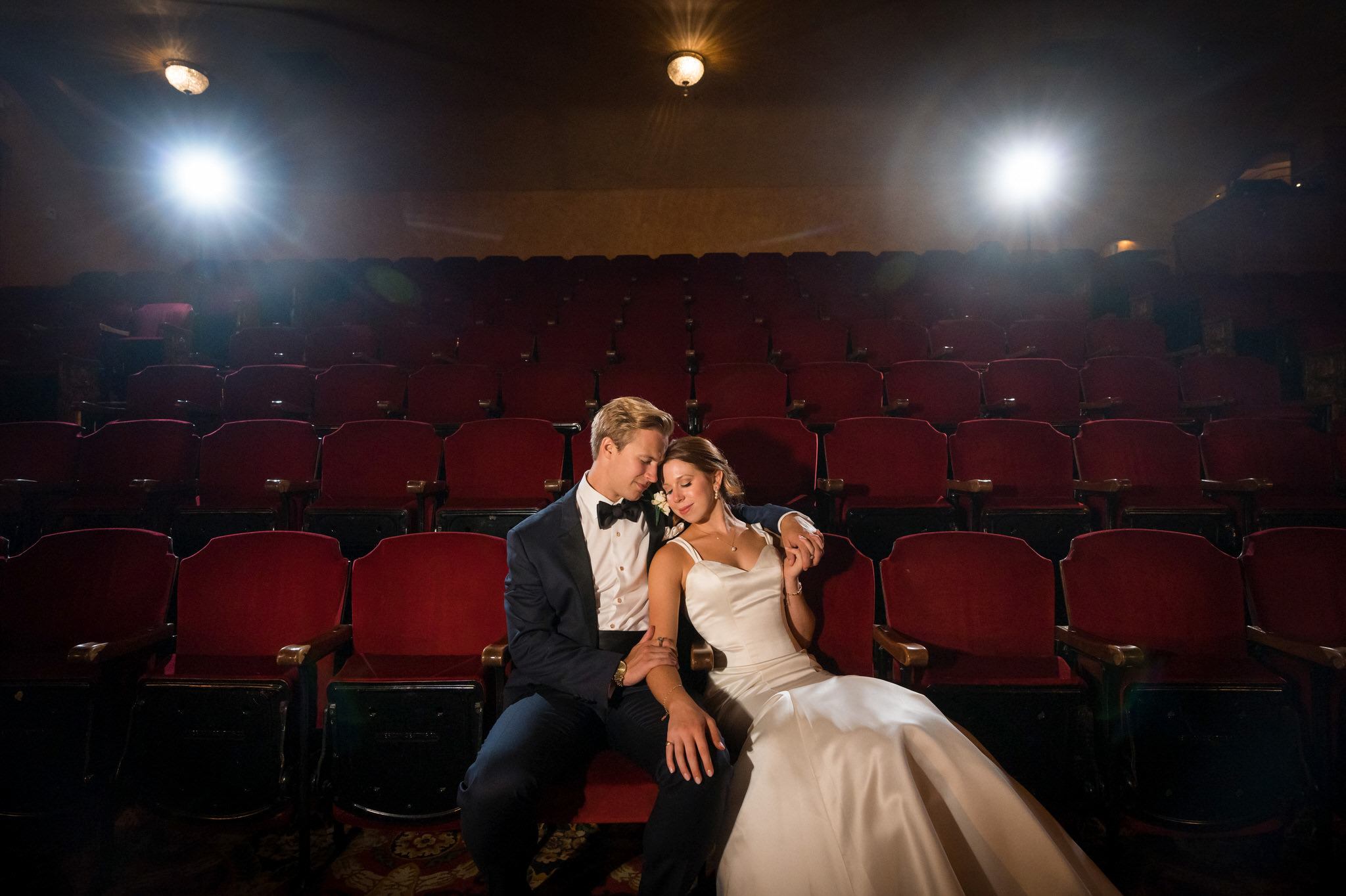 A bride and groom snuggle together sitting in red theatre chairs during their Gem Theatre Detroit wedding reception.  