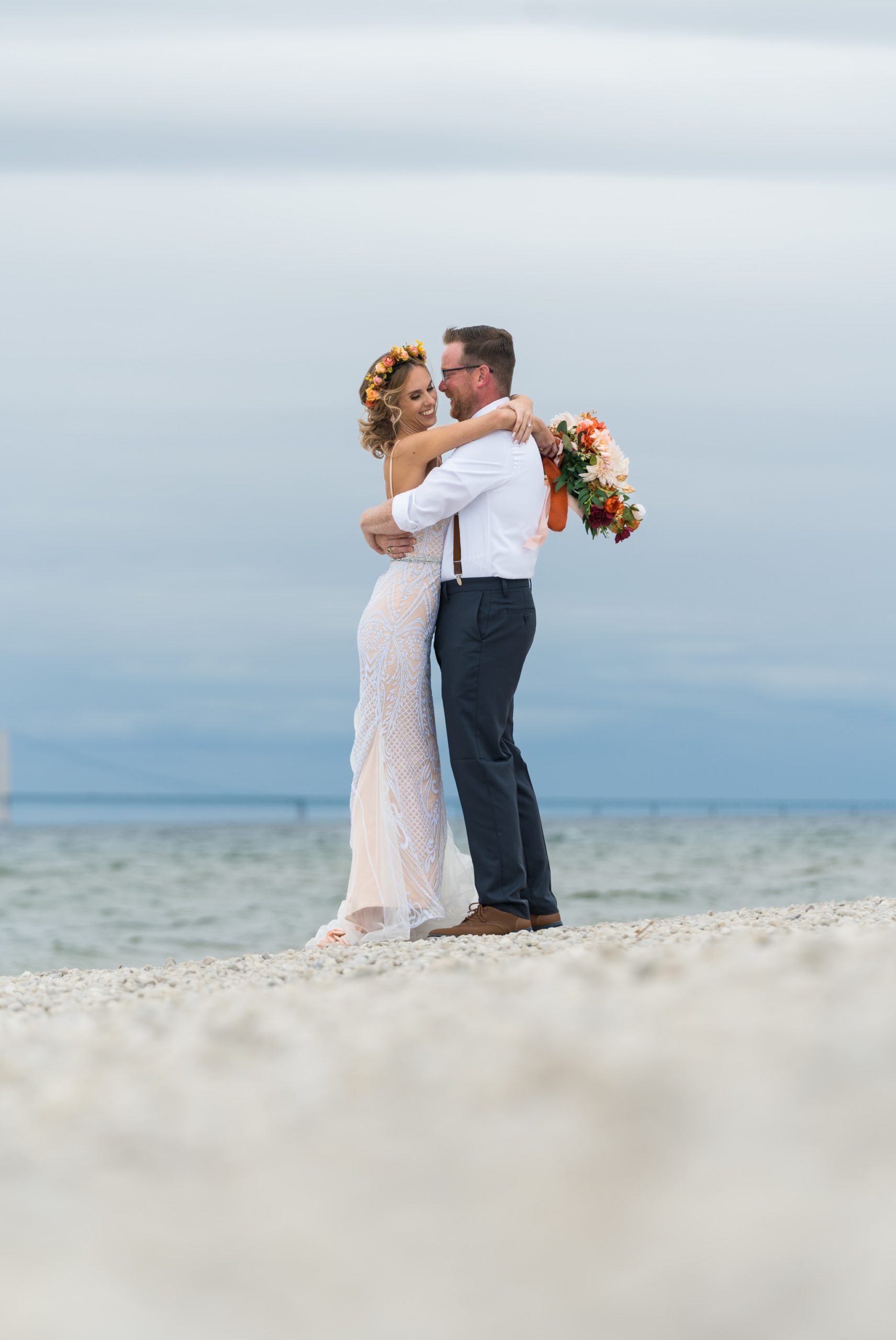 A bride and groom hug with the Mackinac Island bridge in the background.  