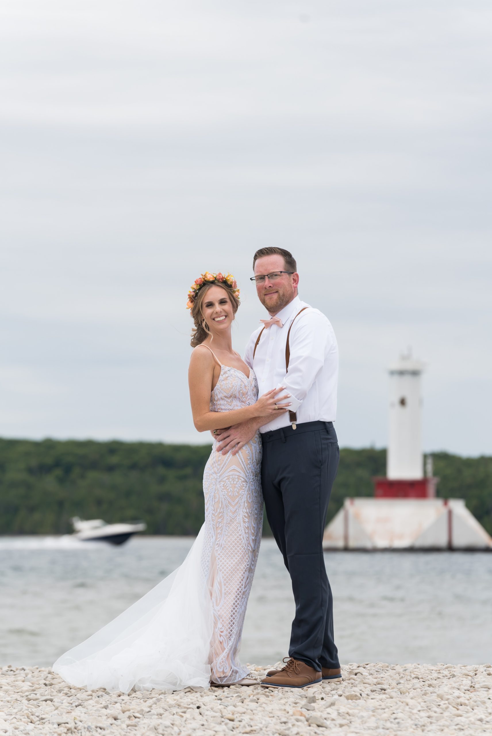 A bride and groom pose on the shores of Mackinac Island with a lighthouse in the background during their Mission Point Resort wedding.  