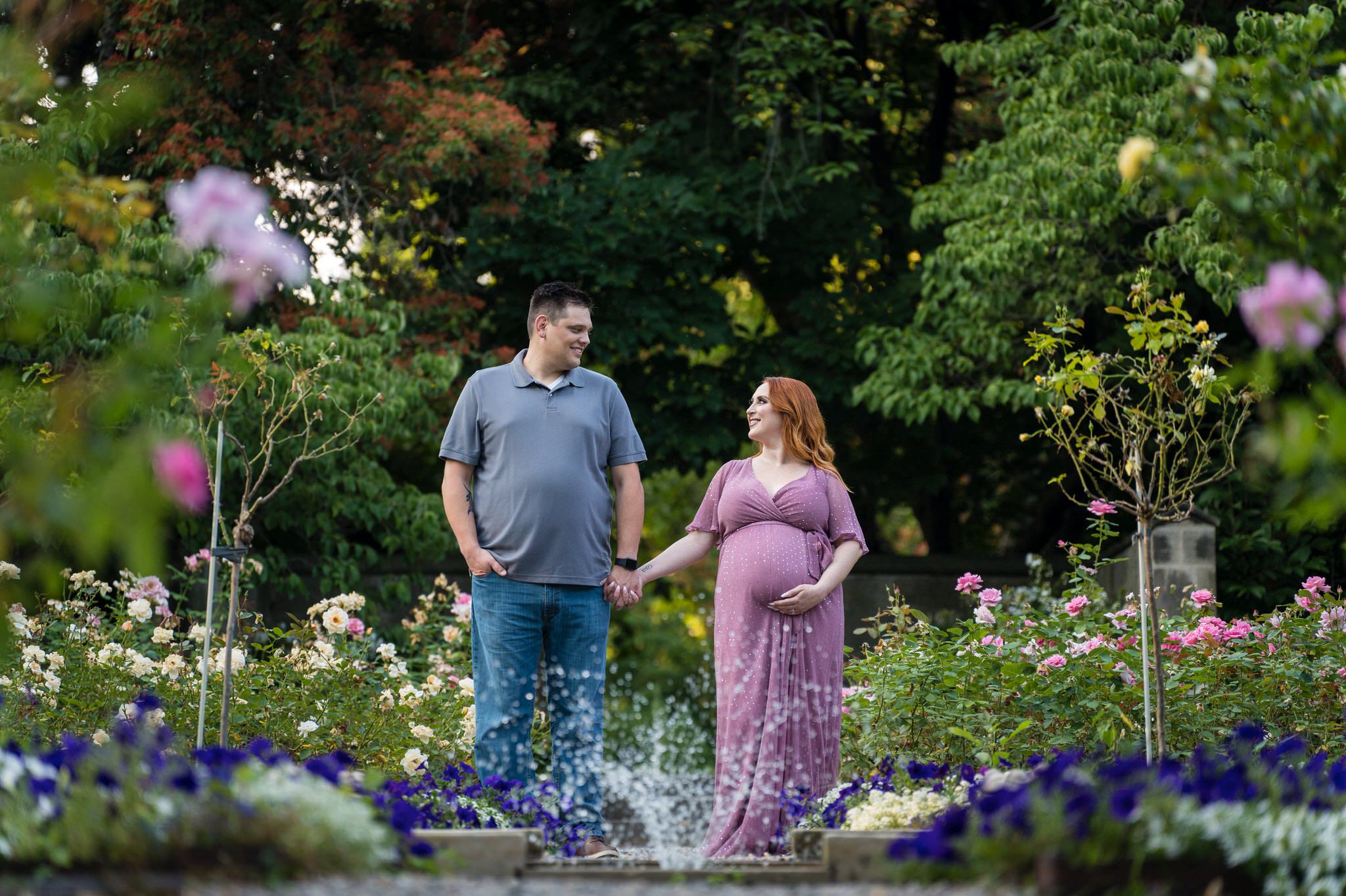 A couple holds hands and looks at each other in the rose garden during their maternity session at Edsel Ford.