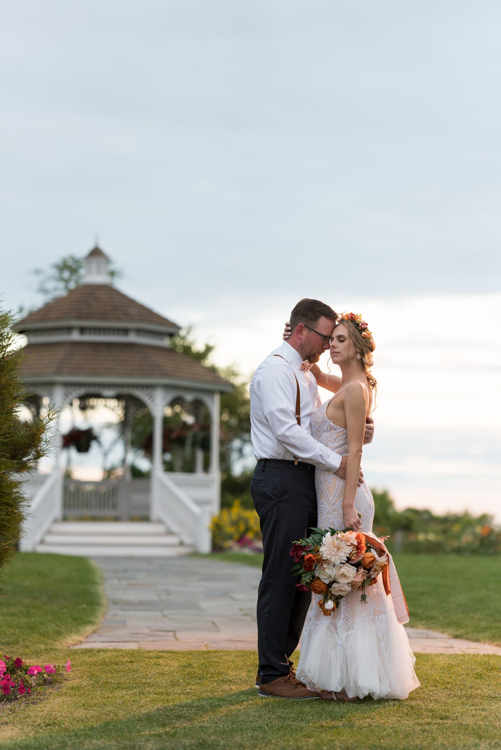 Standing with a gazebo in the background, a bride and groom close their eyes and hold each other at their Mission Pointe Resort wedding.  