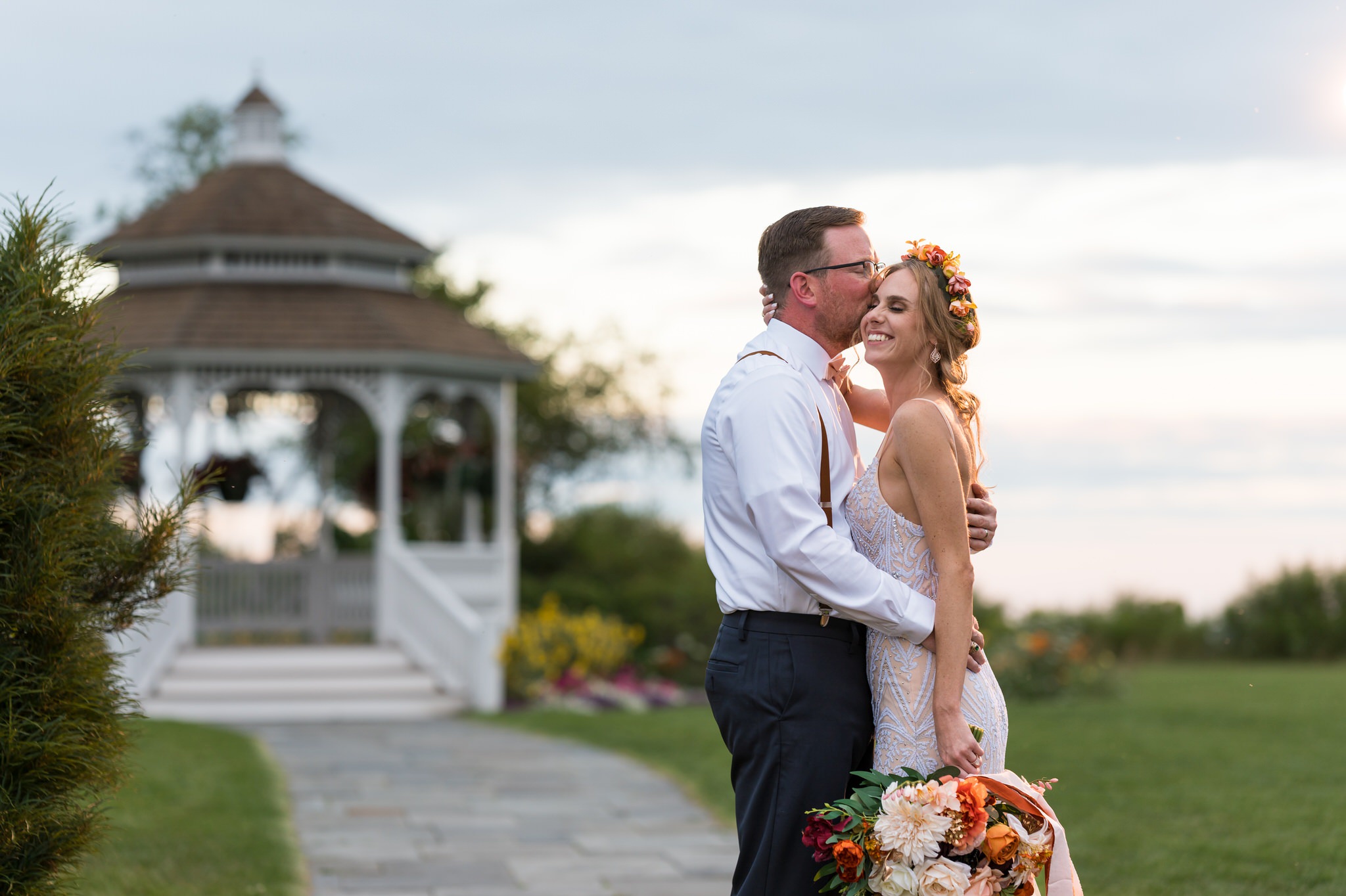 Standing with a gazebo in the background, a groom kisses the temple of his brade at their Mission Pointe Resort wedding.  