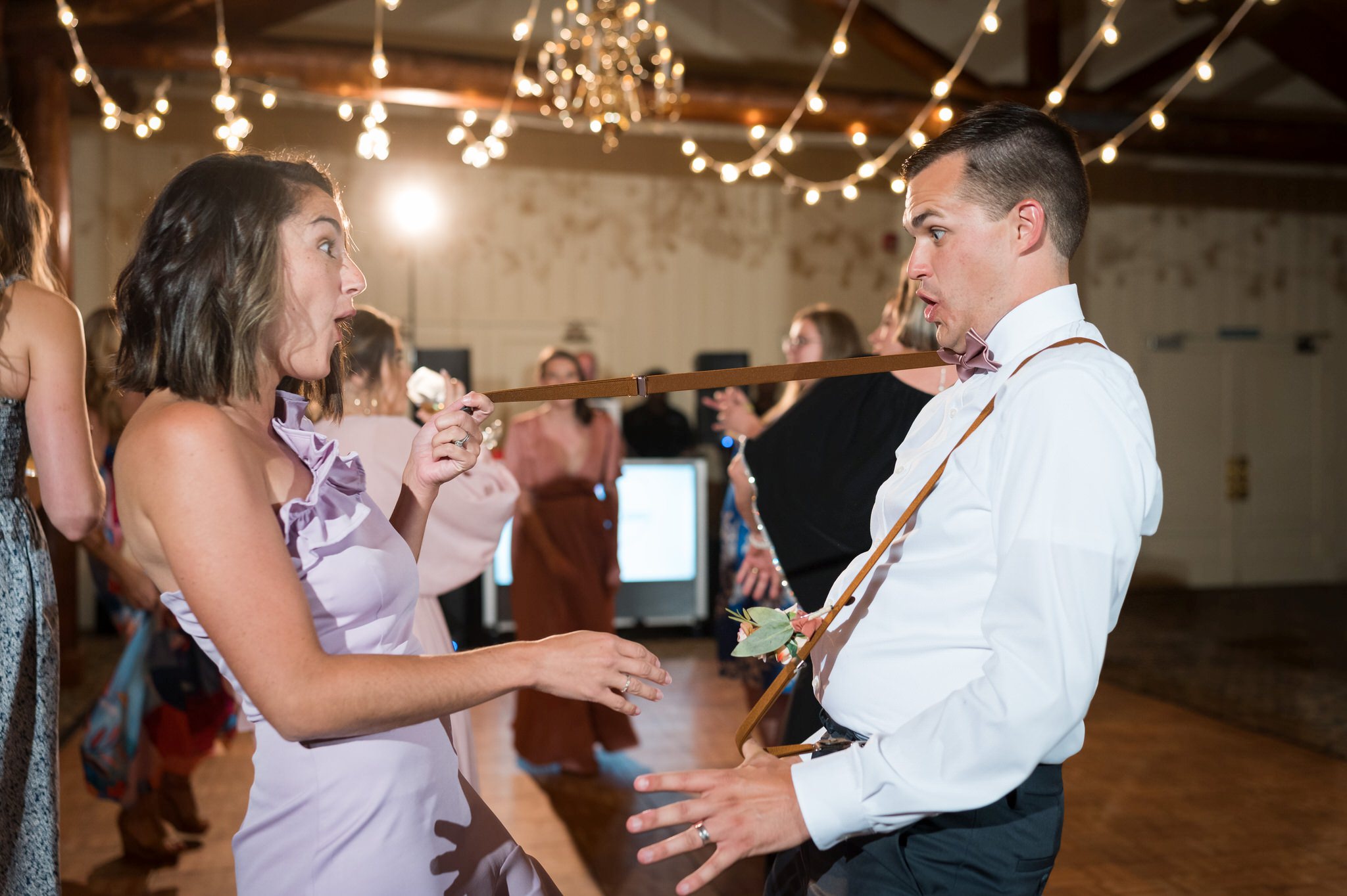 Dancing guests break a groomsman suspender  and look surprised.  