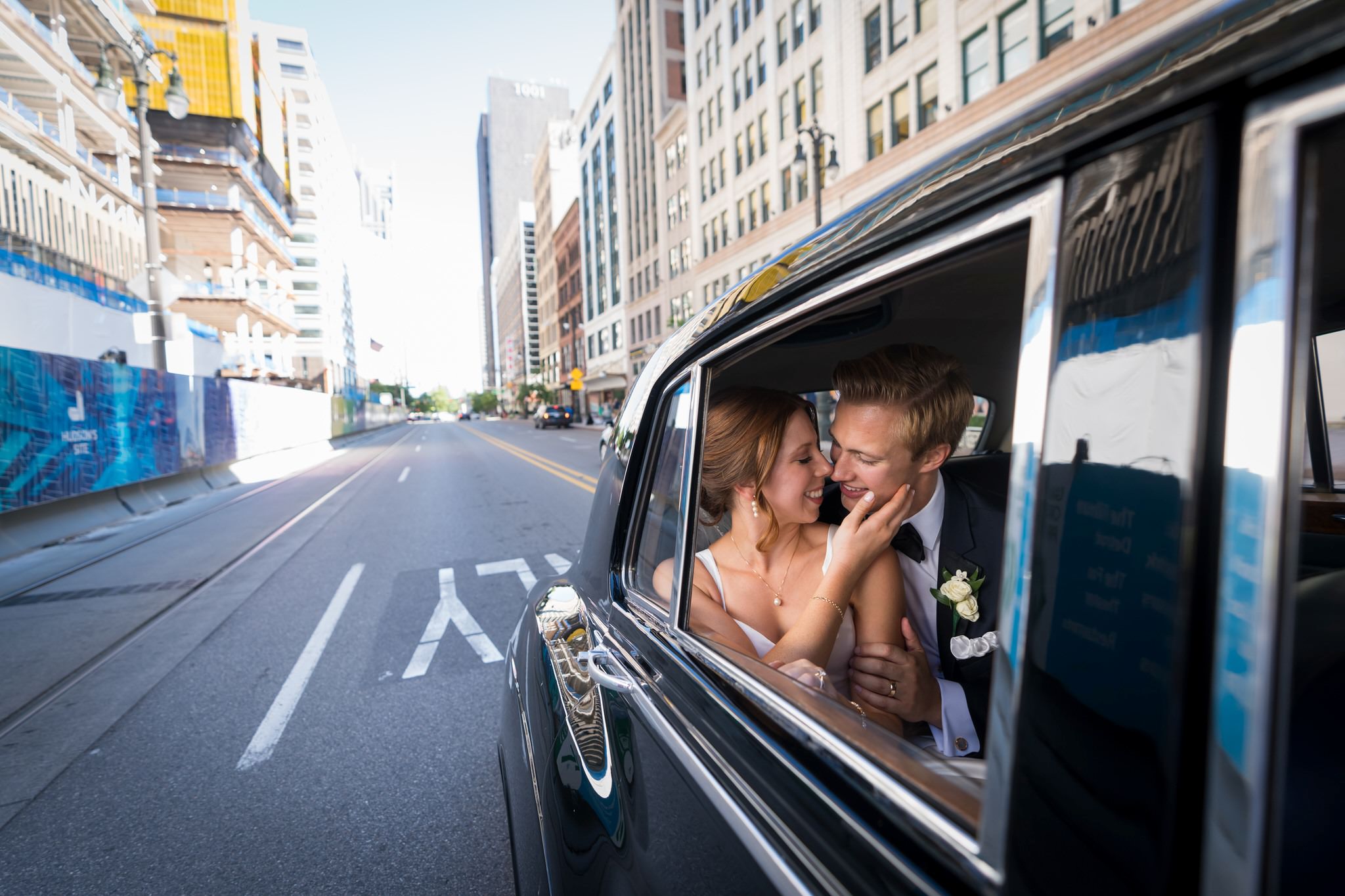 A bride caresses the face of her groom while riding in a Rolls Royce.  