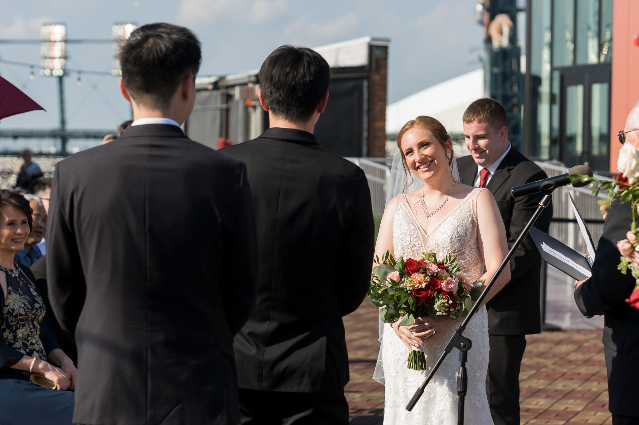 A bride smiles, looking at the groom during the reading of vows, at a rooftop wedding at Detroit Opera House. 