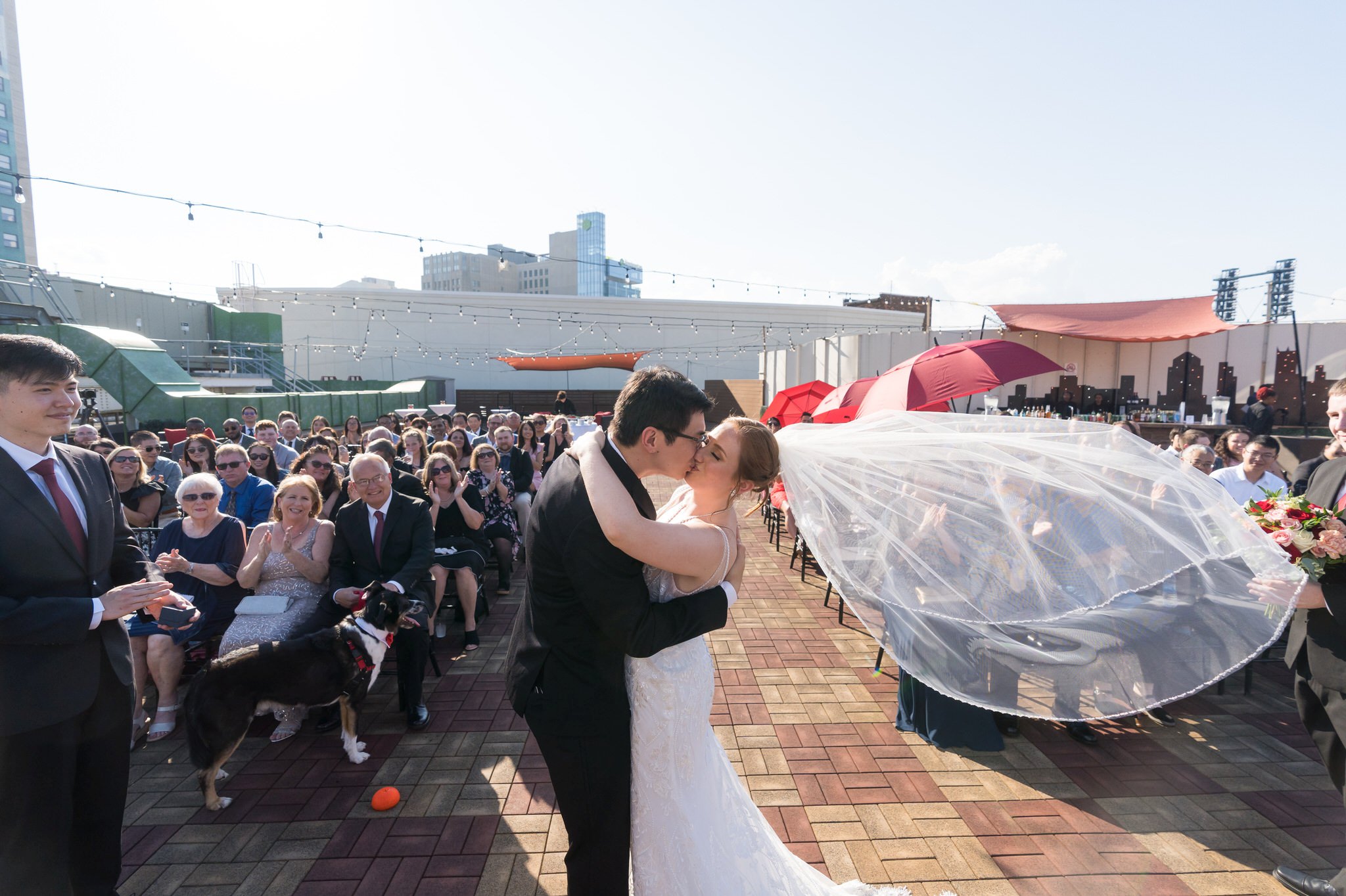 A bride and groom kiss with guests in the background at their rooftop wedding at Detroit Opera House. 