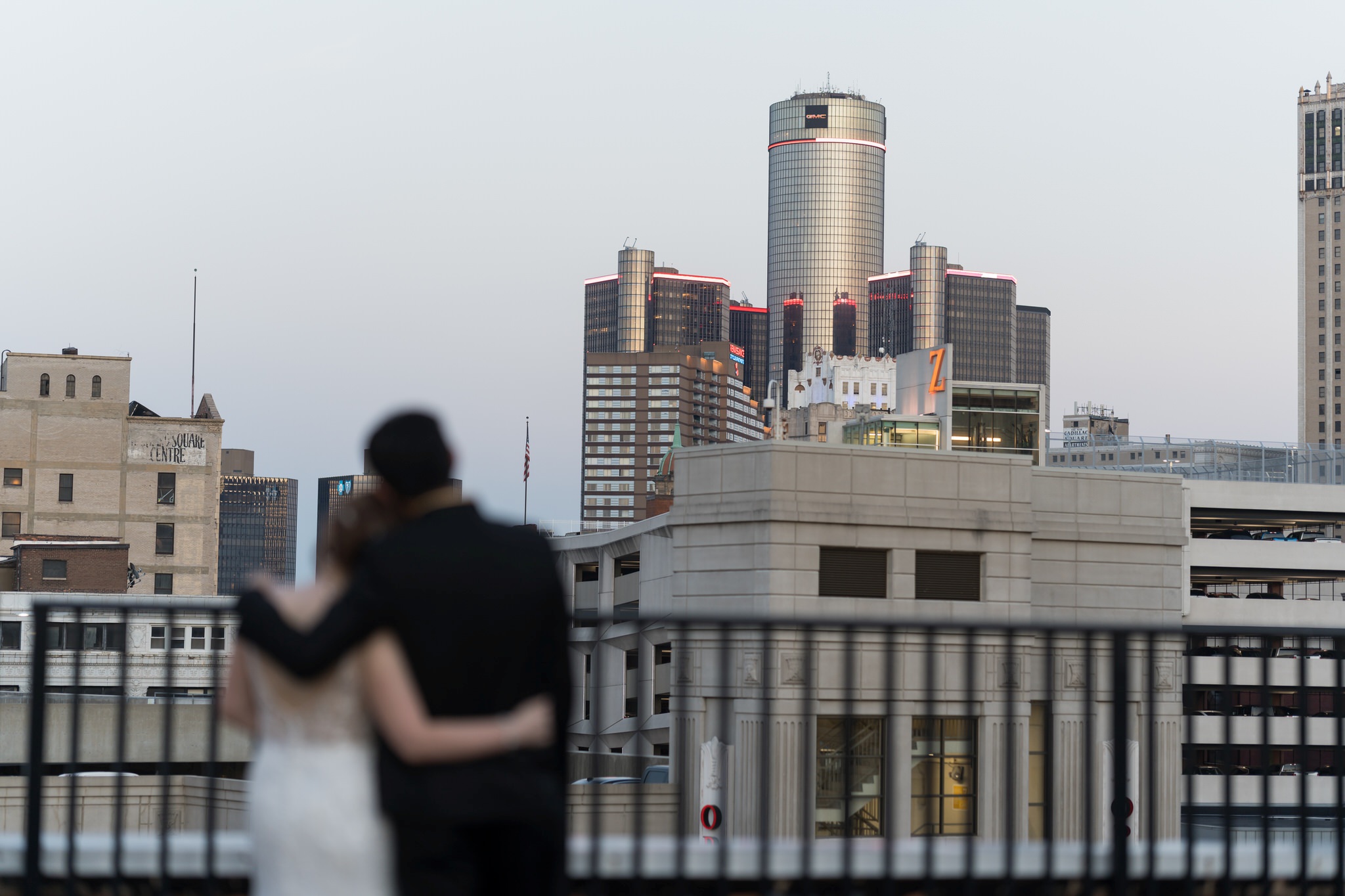 A bride and groom kissing on the rooftop of the Detroit Opera House with the GM Renaissance Center in the background.  