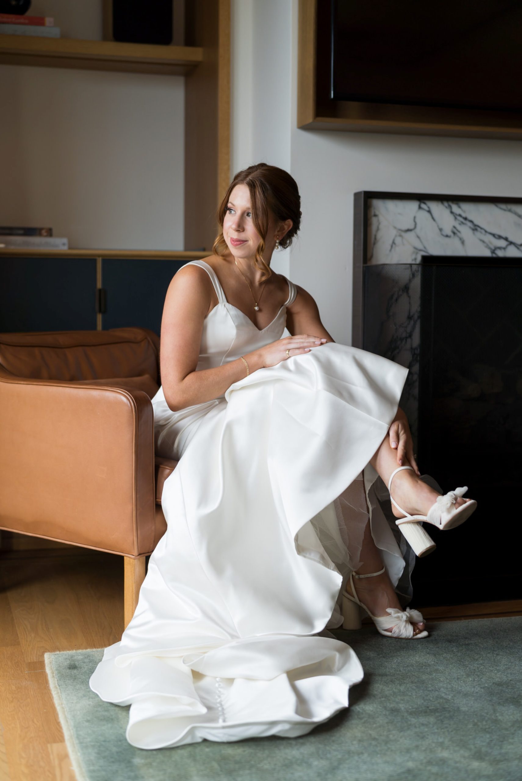 A seated bride looks out the window while adjusting her shoe at the Shinola Hotel in Detroit. 