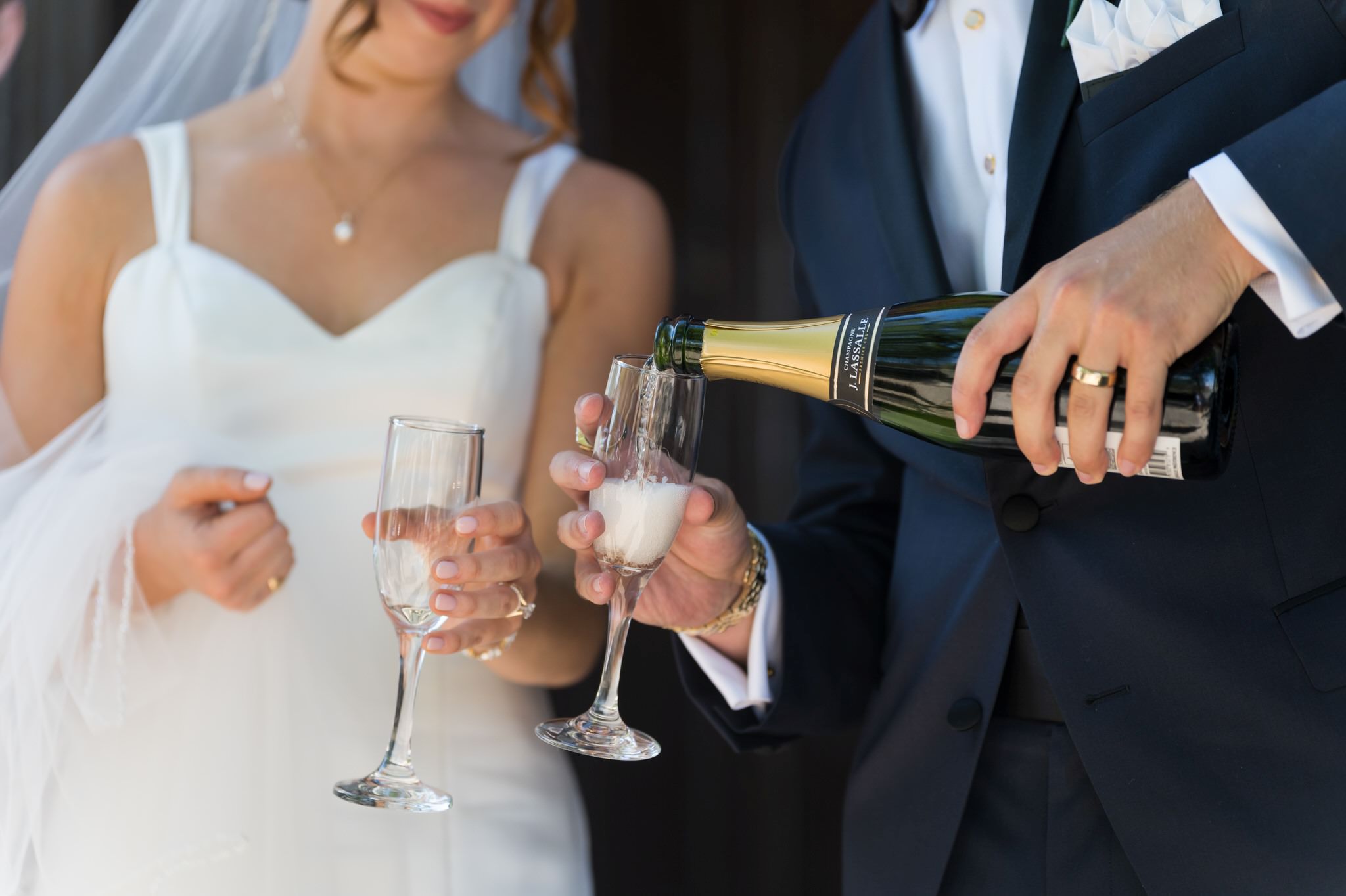 Champagne is poured into flutes with the bride and groom in the background.  