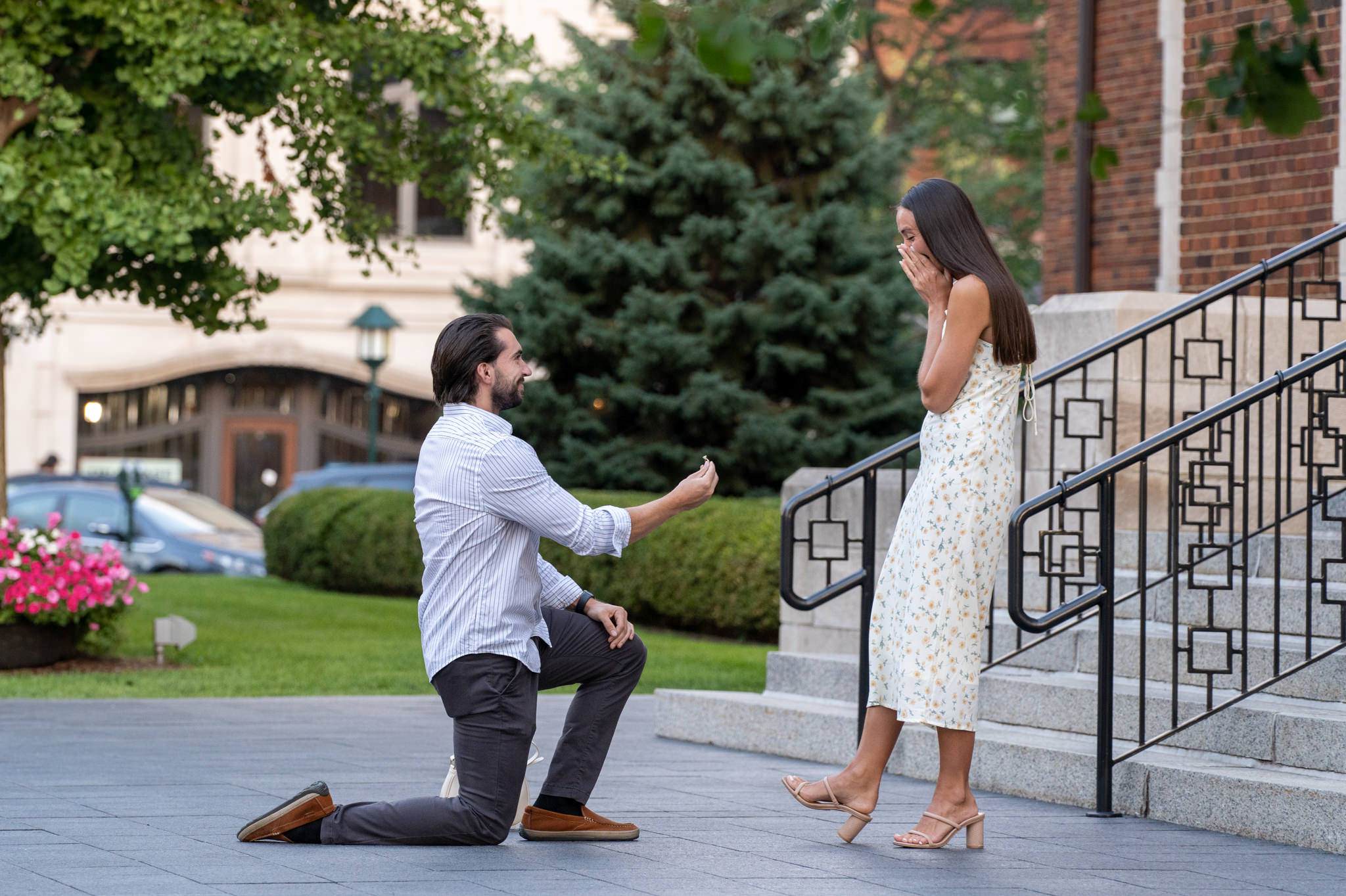 man takes a knee and proposes in a downtown Birmingham proposal as his fiance covers her mouth in excitement