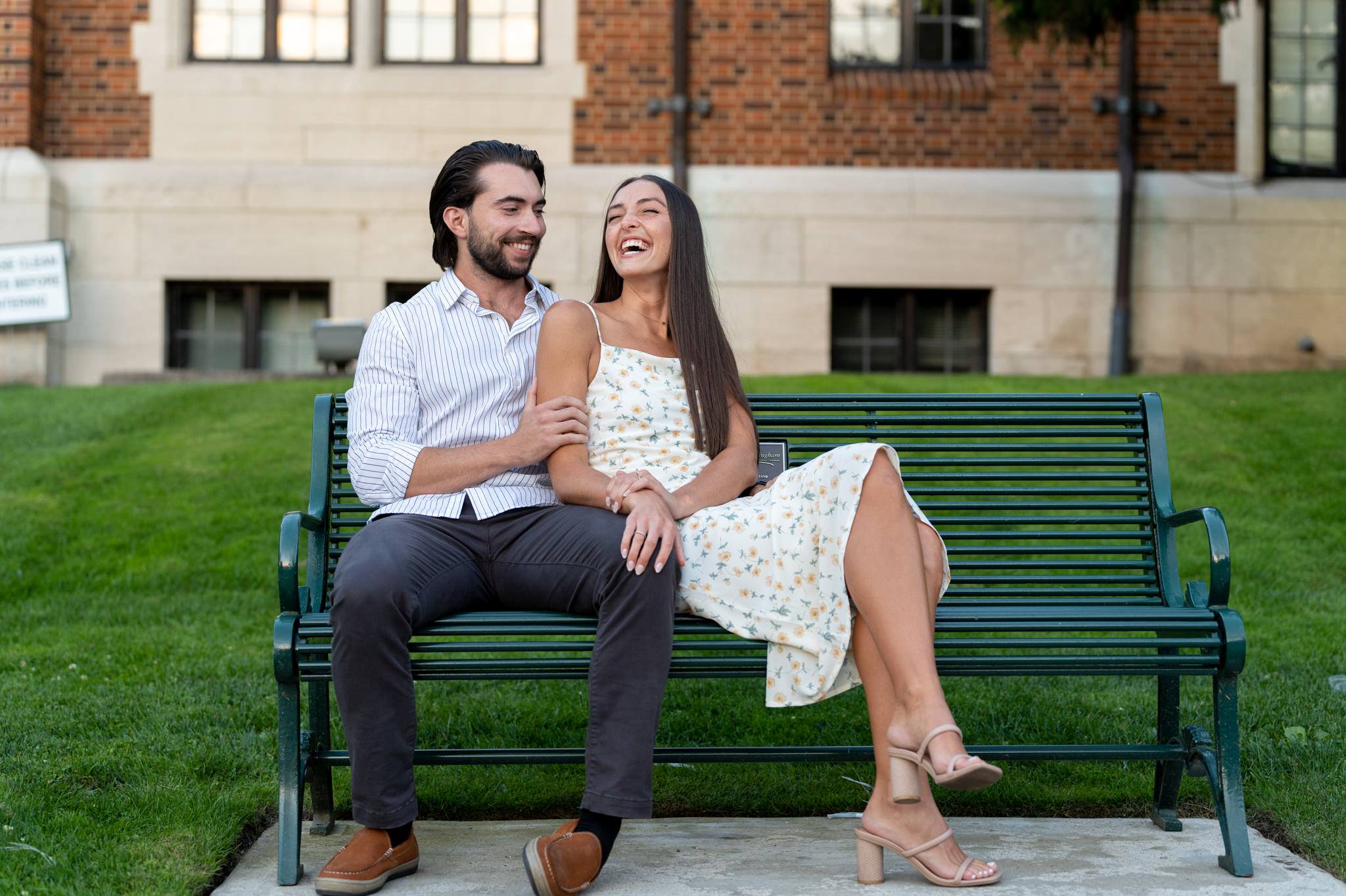 a couple, sitting on a green bench, smile and laugh in downtown Birmingham, Michigan