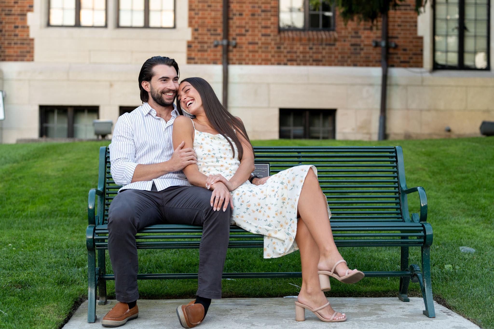 a couple, sitting on a green bench, smile and laugh in downtown Birmingham, Michigan