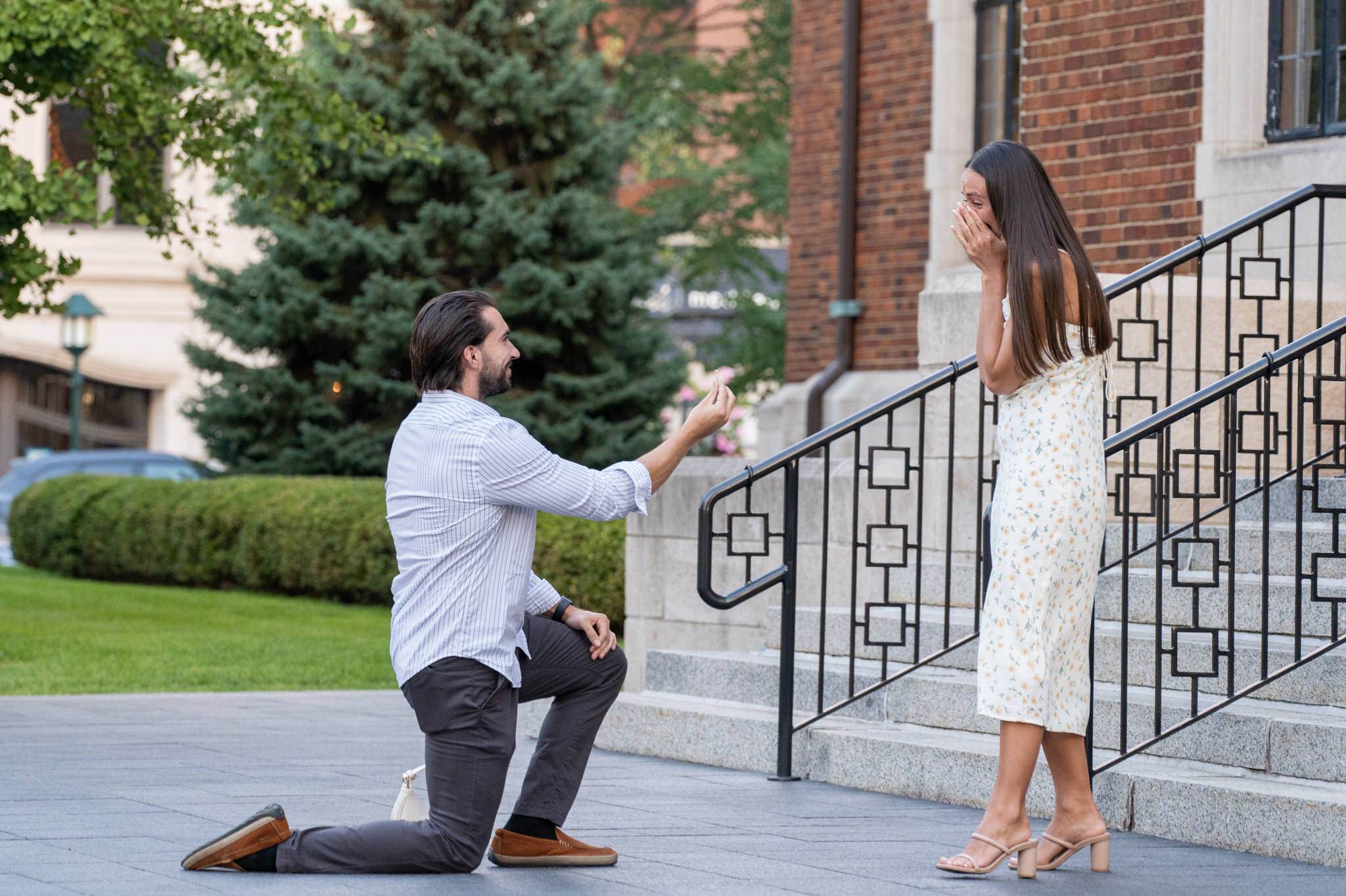 man takes a knee and proposes in a downtown Birmingham proposal as his fiance covers her mouth in excitement