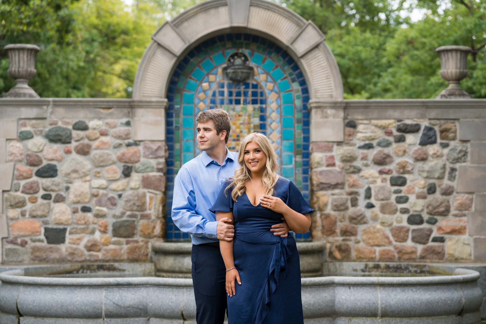 A couple look at each other with a blue fountain behind them during their Cranbrook engagement session. 