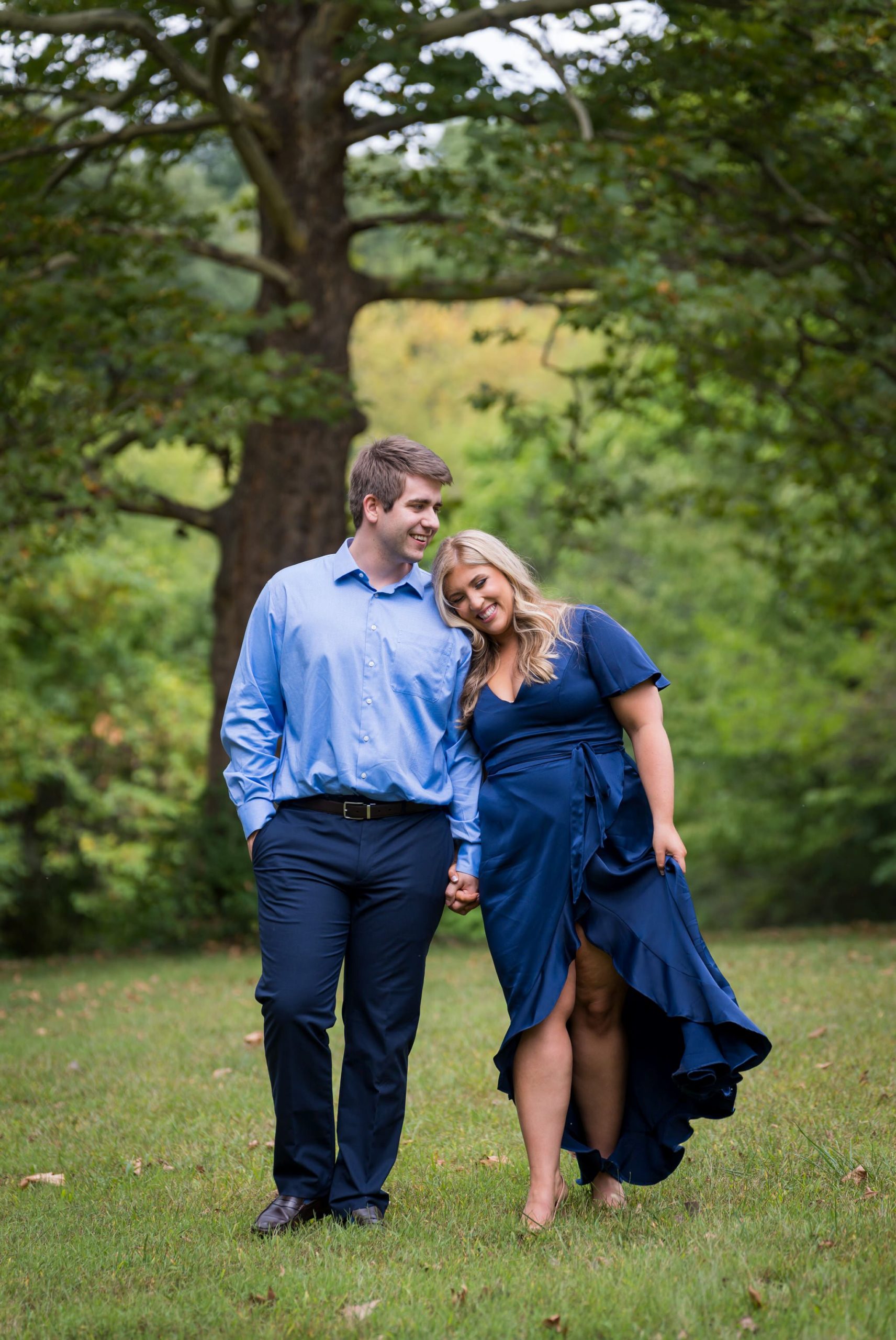 A couple, dressed in blue, hold hands and walk during their Cranbrook engagement session.  